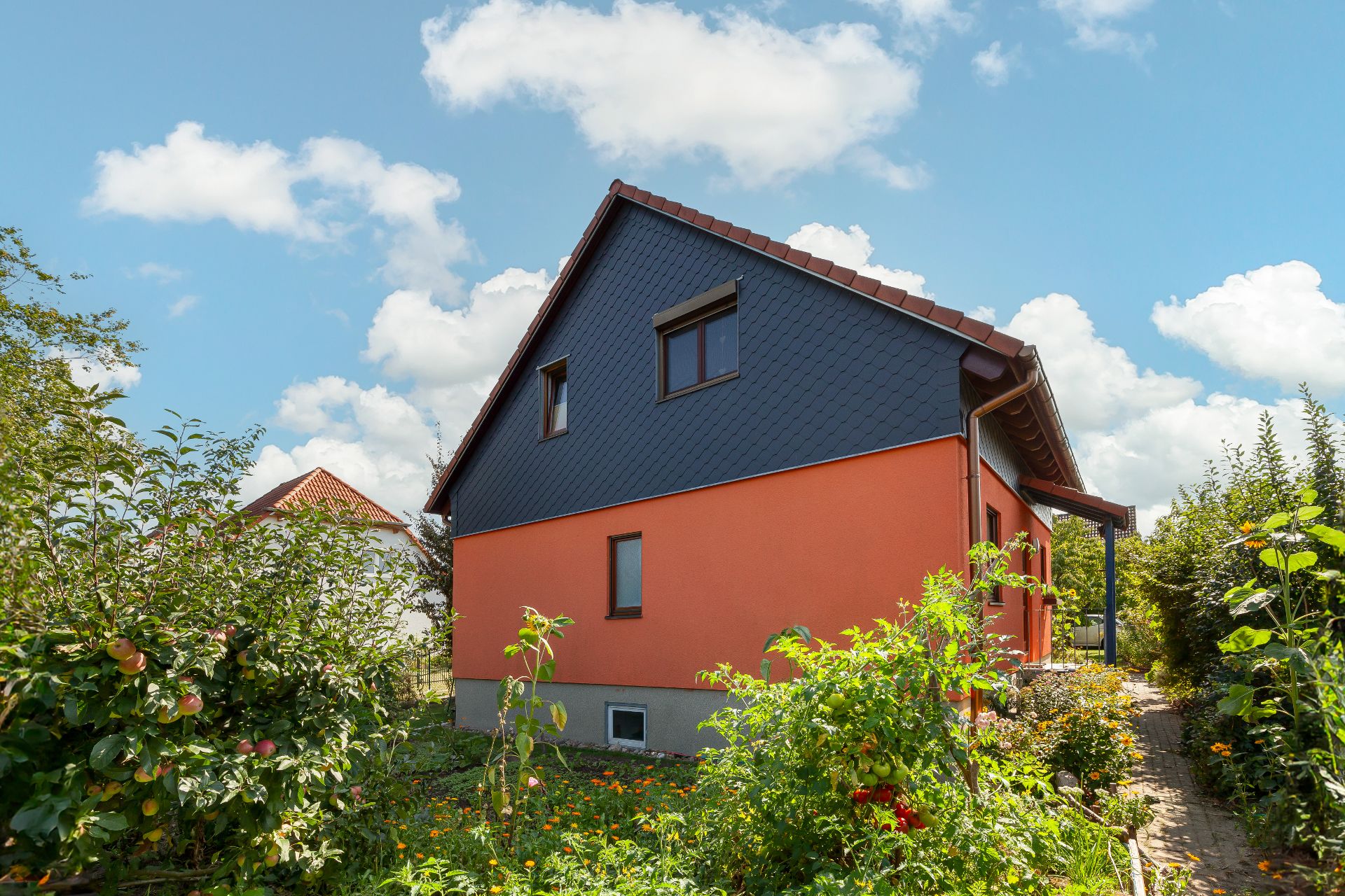 Haus mit orangefarbener Fassade und Garten mit Pflanzen und Blumen bei Sonnenschein.