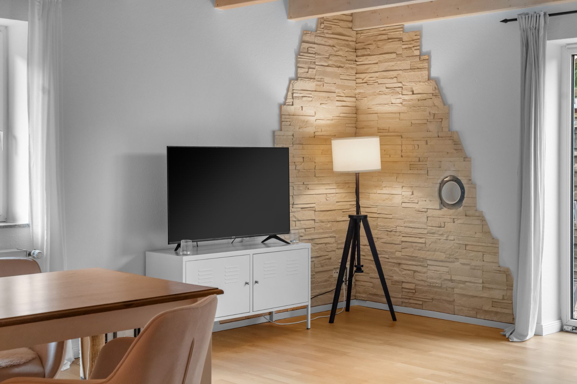 Wohnzimmer mit Fernseher auf weißem Schrank, Stehlampe und gemauerter Wand in der Ecke.
