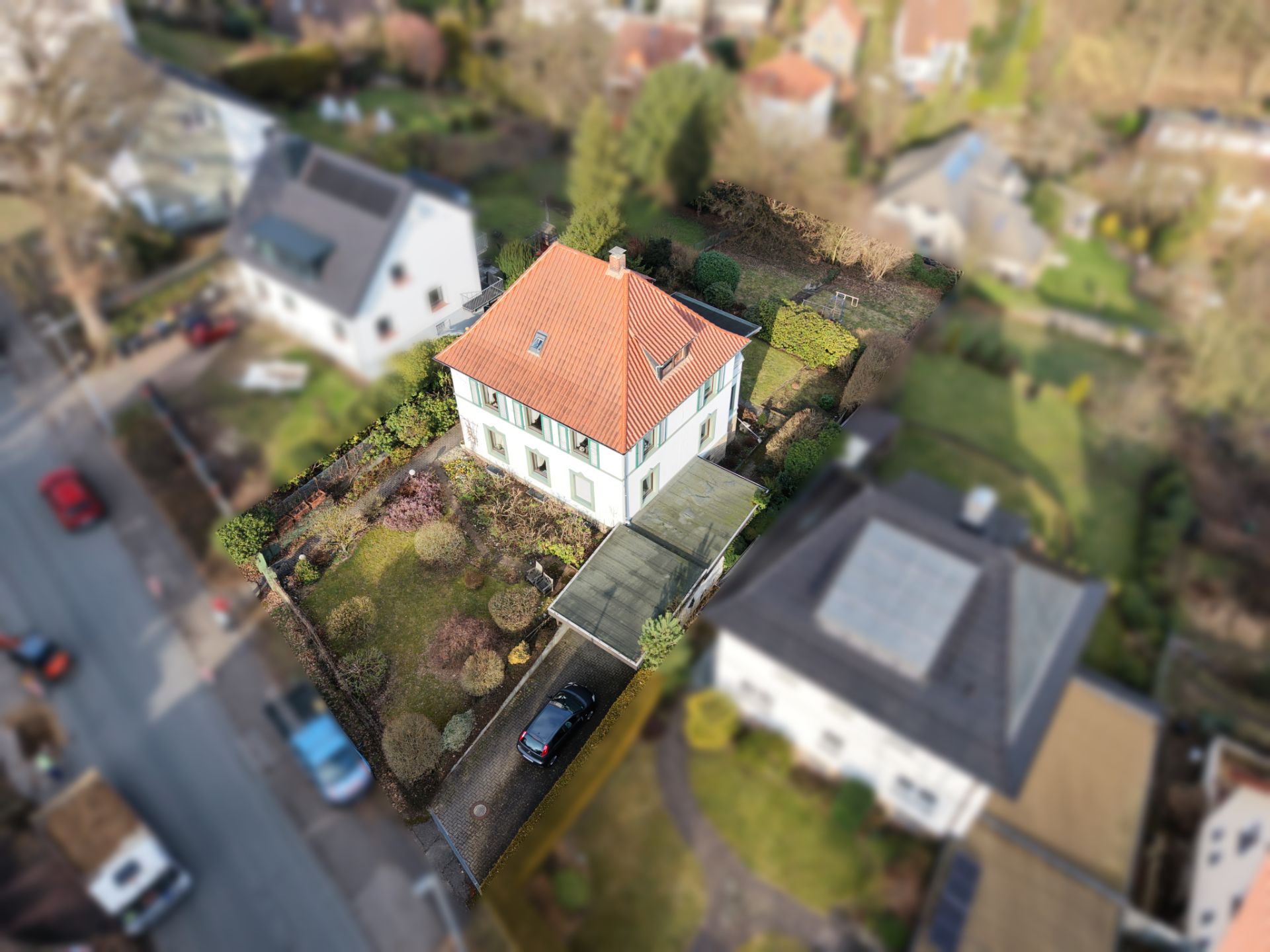 Luftaufnahme eines Wohnhauses mit rotem Dach, Garten und Einfahrt mit Auto.