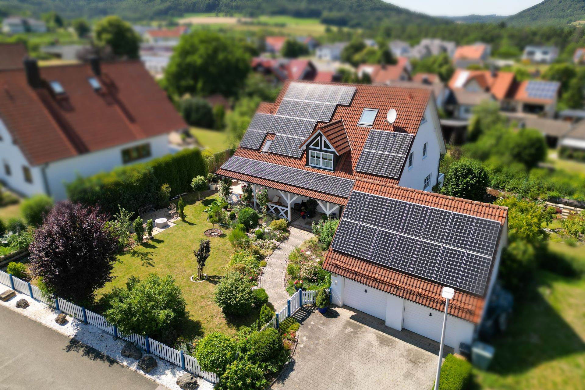 Haus mit Solarpaneelen auf dem Dach und gepflegtem Garten, umgeben von Zaun.