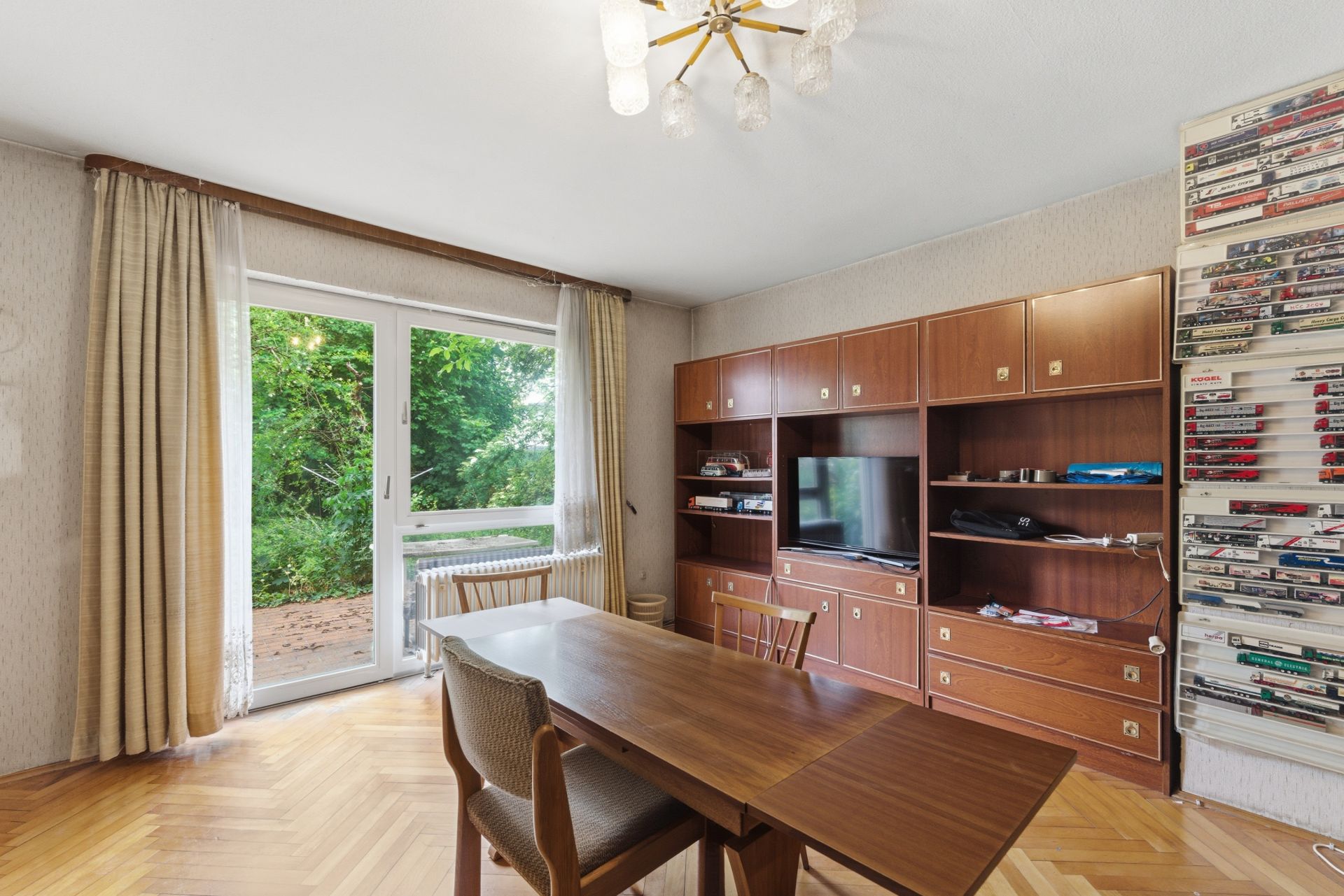 Wohnzimmer mit Holztisch, Stühlen, Wohnwand, Regal und Blick auf Terrasse und Garten.
