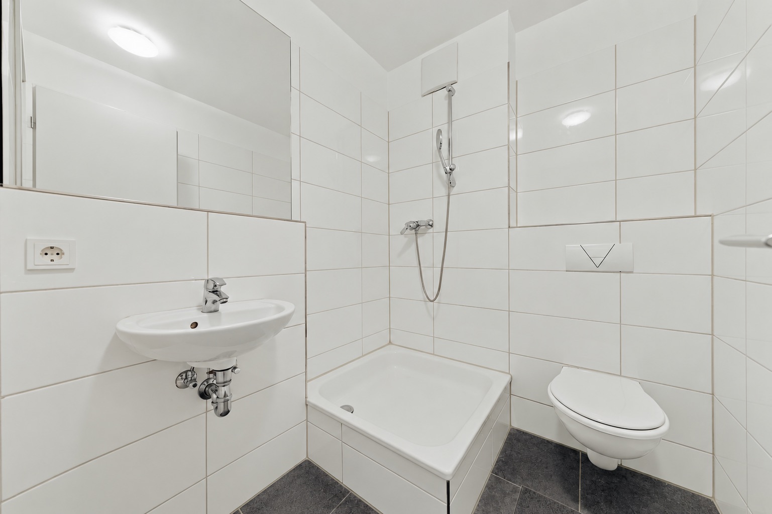Modernes, weiß gefliestes Bad mit Dusche, Waschbecken und Wandtoilette.