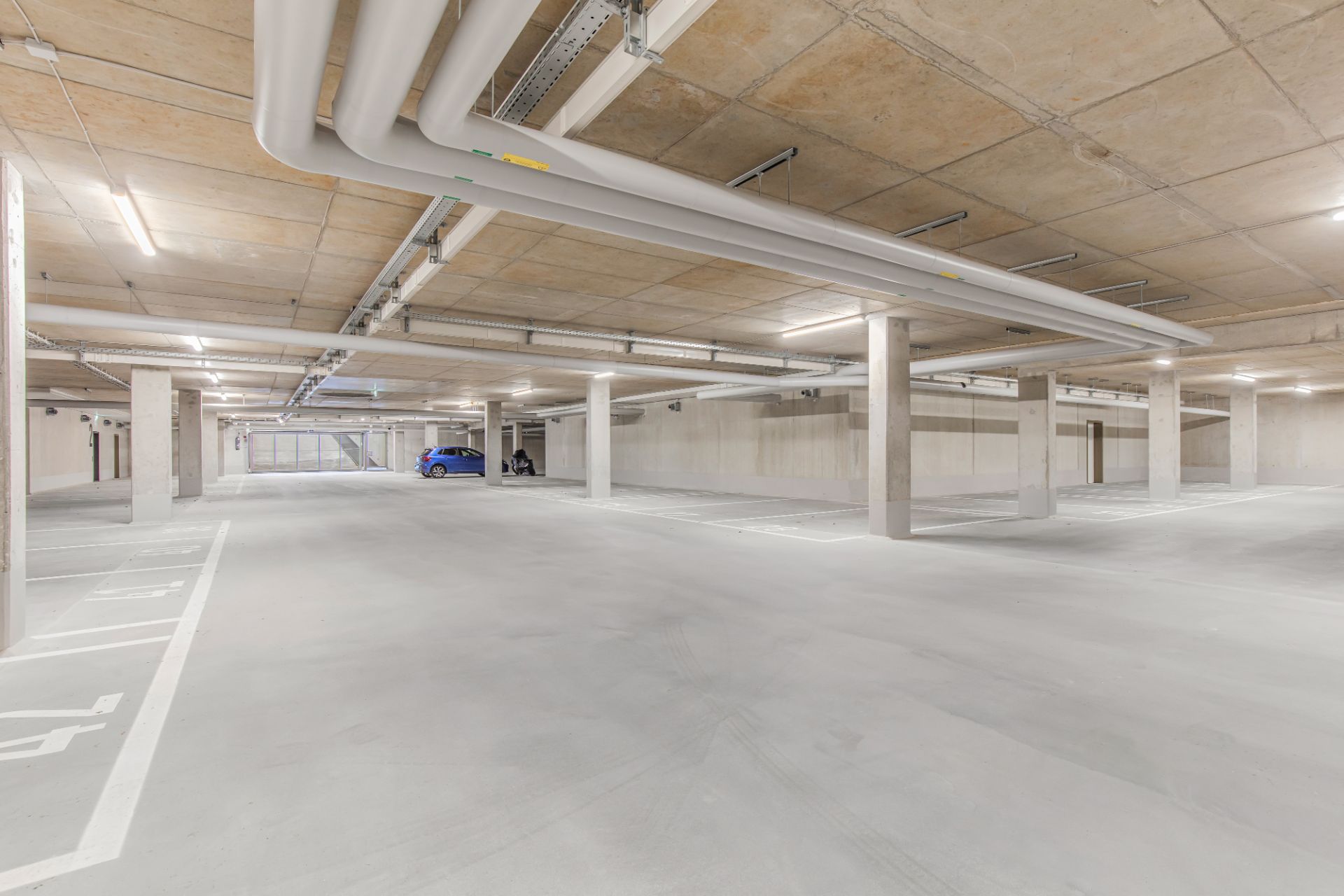 Helle Tiefgarage mit markierten Parkplätzen, wenigen Autos und Betonpfeilern.