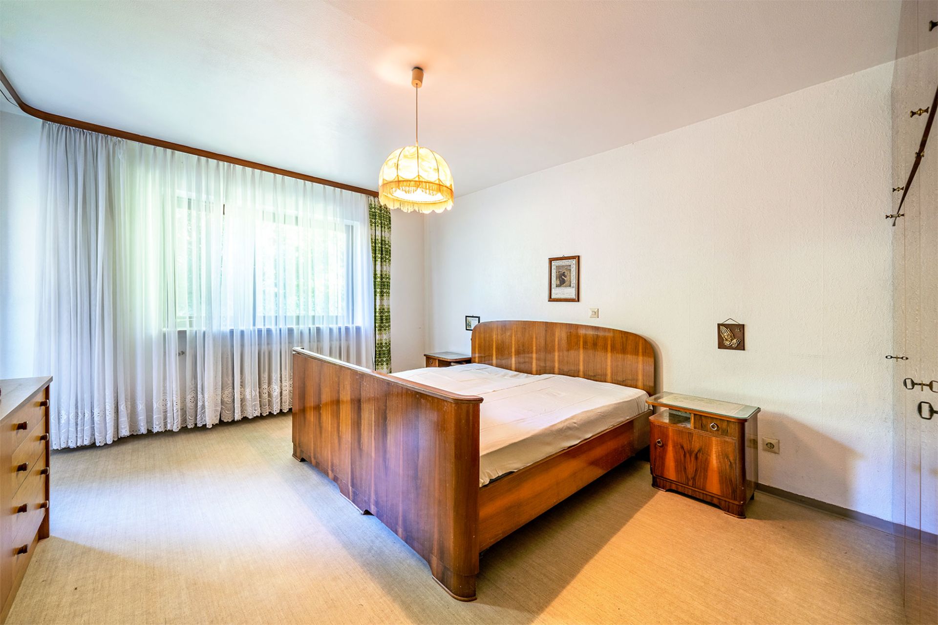 Helles Schlafzimmer mit Holzbett, Nachttischen und großem Fenster mit weißen Vorhängen.