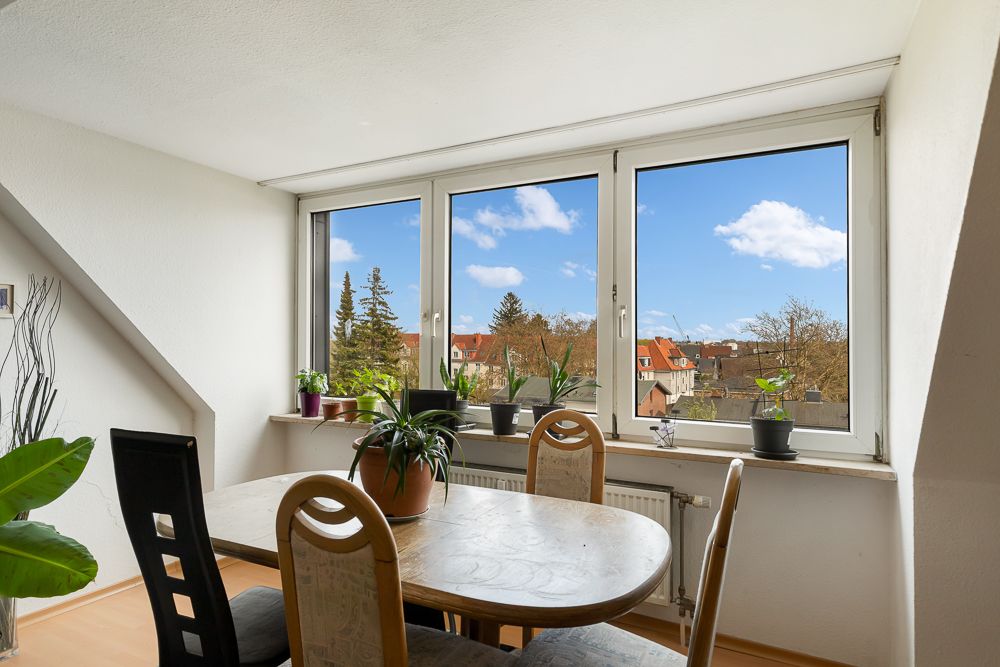 Essbereich mit Holztisch, Stühlen und Pflanzen vor einem großen Fenster mit Blick ins Freie.