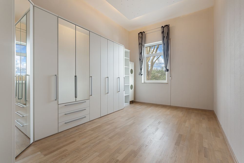 Leeres Zimmer mit großem weißen Kleiderschrank, Holzfußboden und Fenster mit Vorhängen.