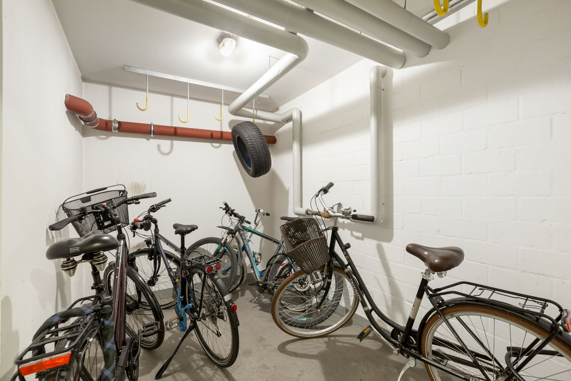 Fahrradraum mit mehreren abgestellten Fahrrädern und gelben Haken an der Decke.