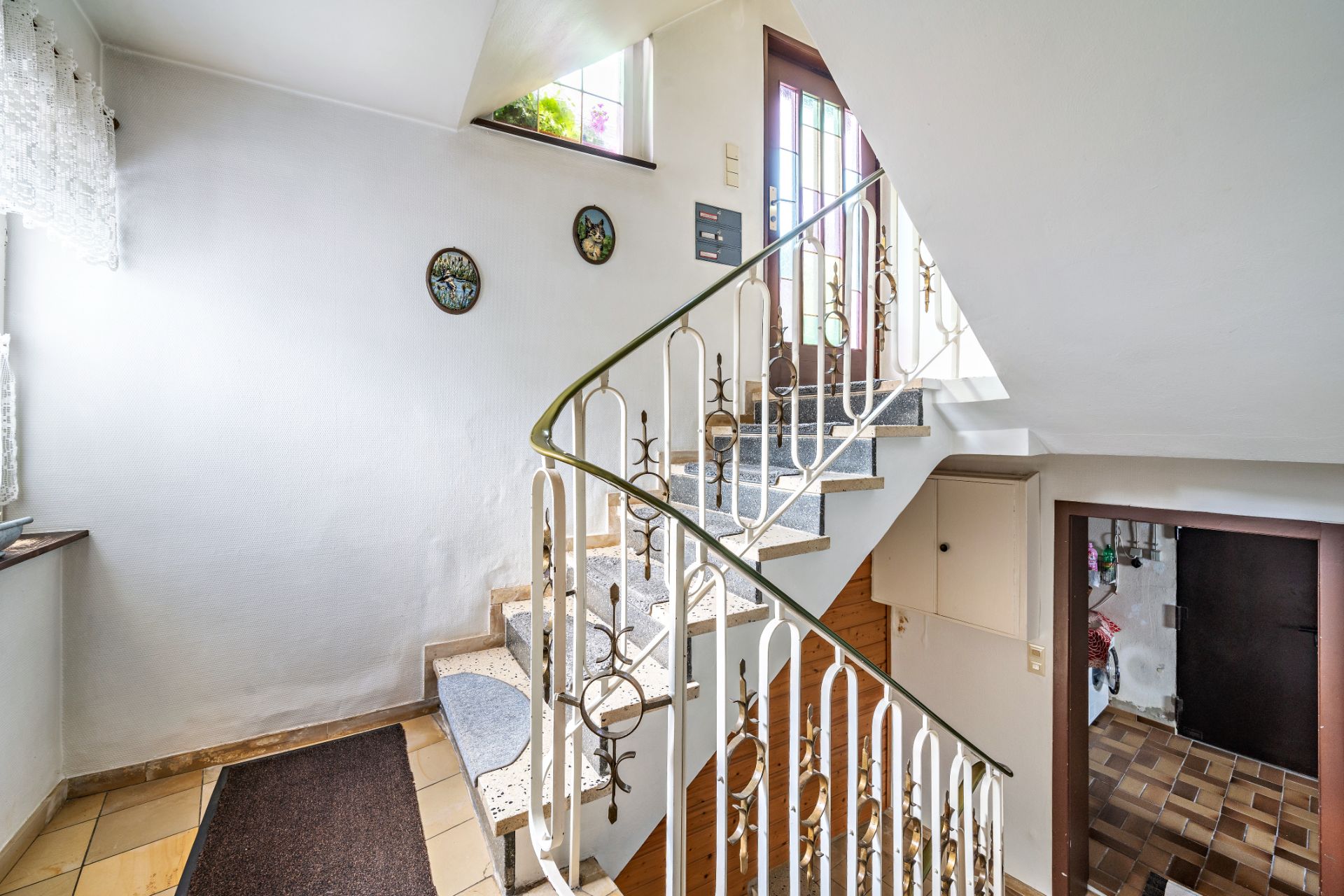 Helles Treppenhaus mit Metallgeländer und Fliesenboden in einem Wohnhaus.