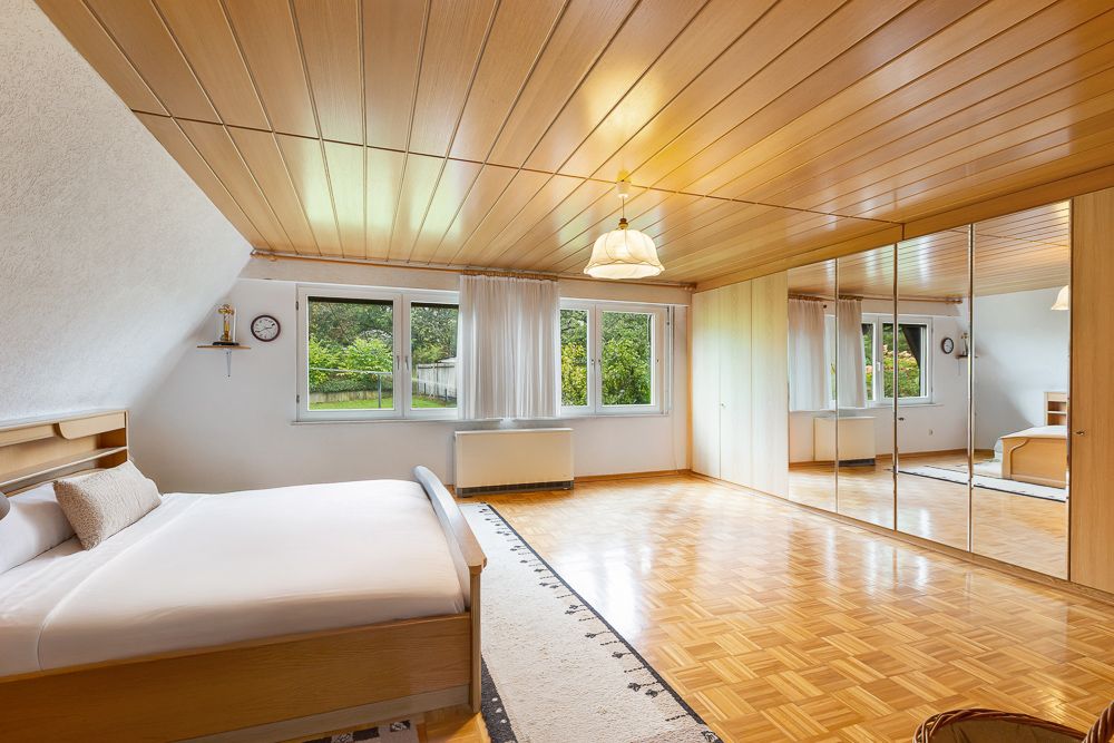 Helles Schlafzimmer mit Holzboden, großem Bett, Spiegelkleiderschrank und Fenstern mit Blick ins Grüne.