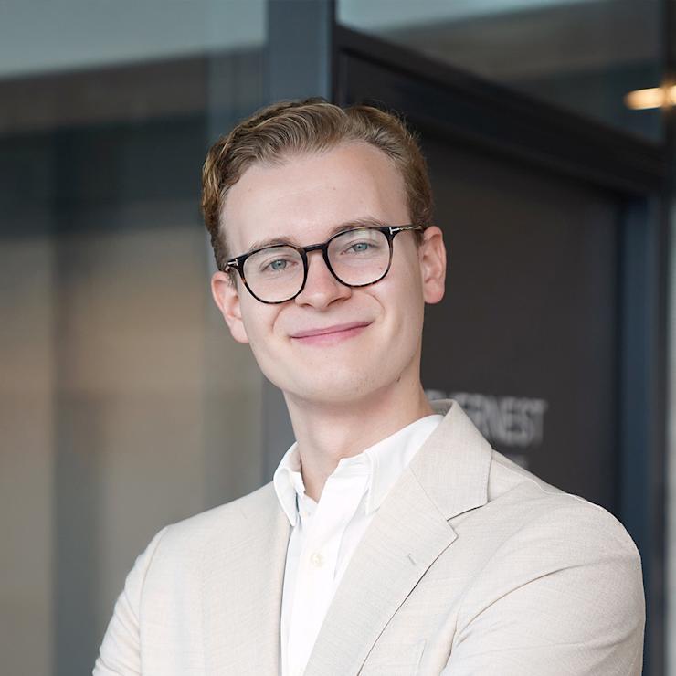 Junge Person mit Brille und weißem Pullover steht vor einer Glastür.