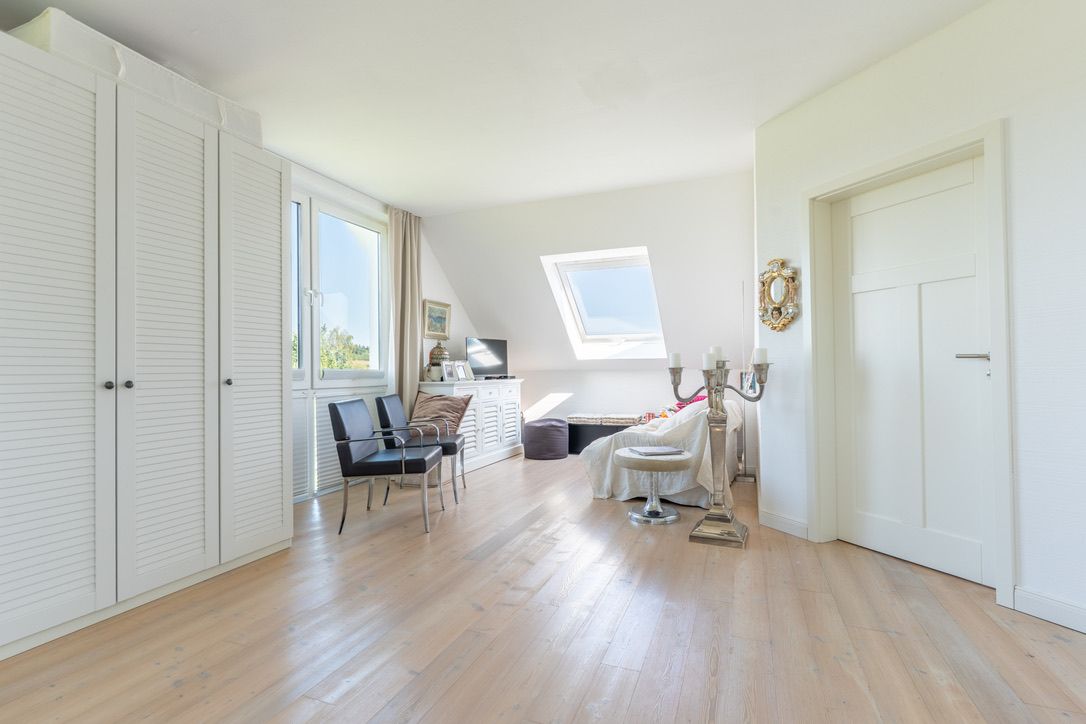 Helles Wohnzimmer mit Holzfußboden, weißen Möbeln, Sesseln und großem Fenster.
