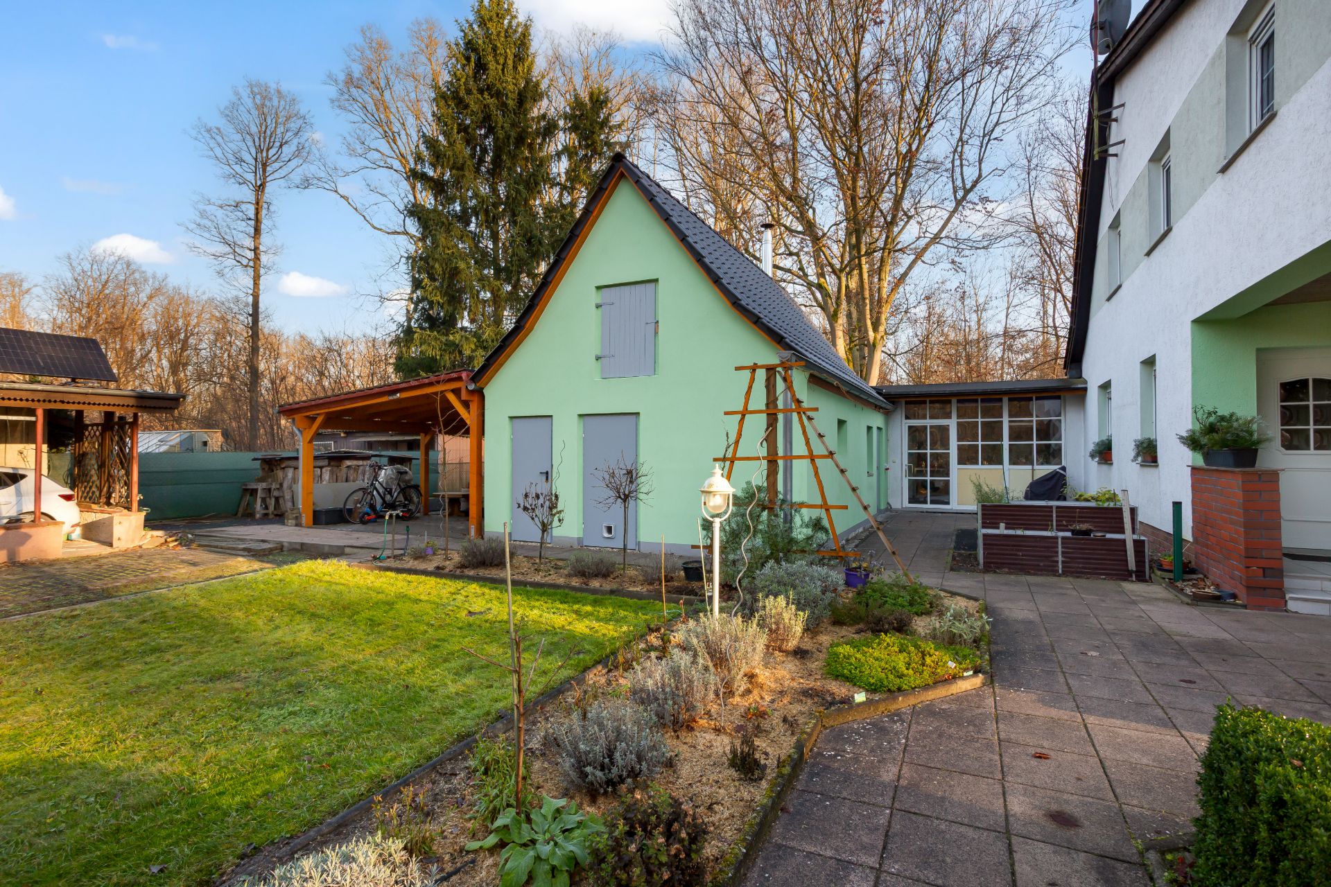 Garten mit Rasen, Blumenbeet und hellgrünem Haus mit geschlossenem Fensterläden.