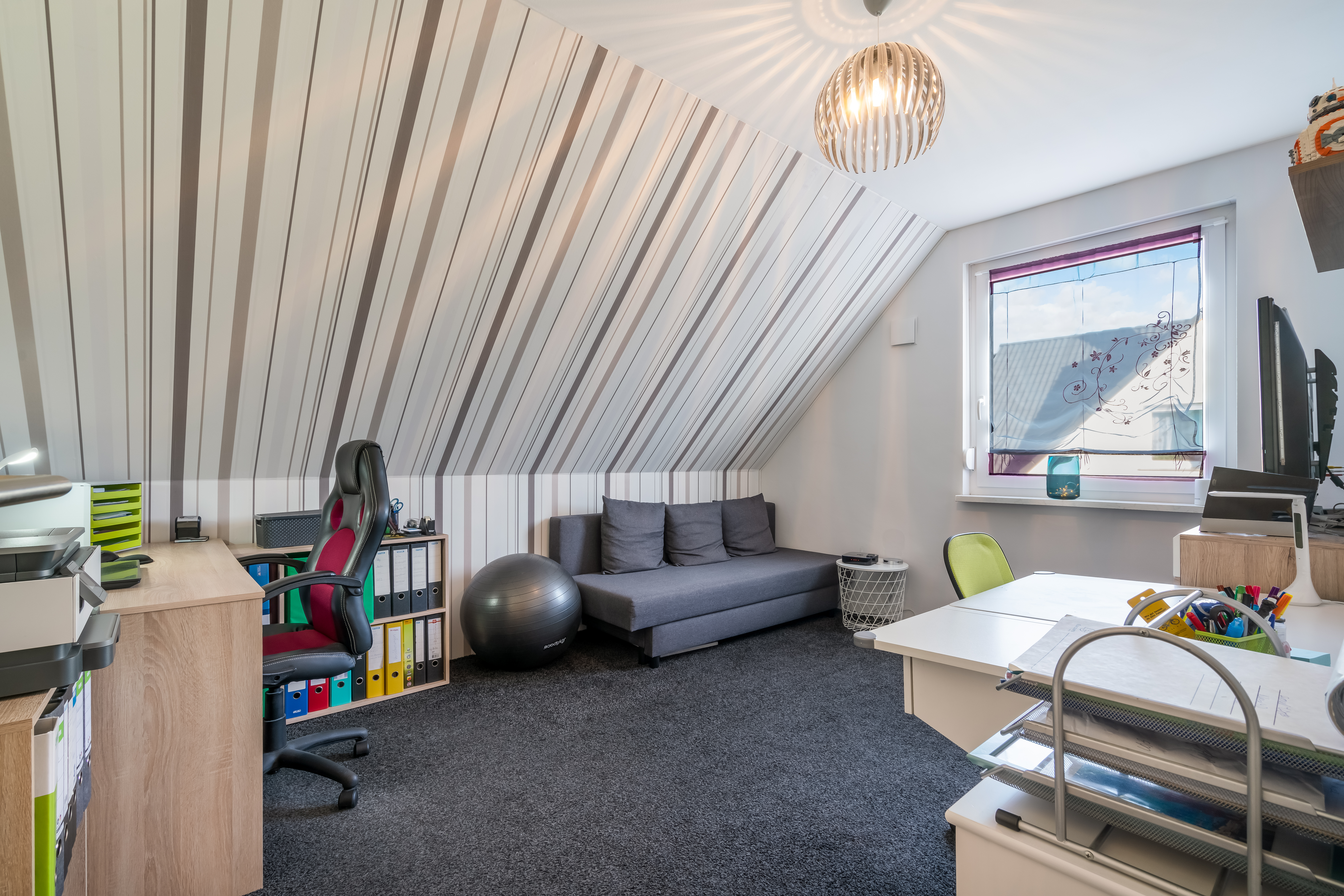 Modernes Arbeitszimmer mit Schreibtisch, Sofa, Bürostuhl und Fenster im Dachgeschoss.