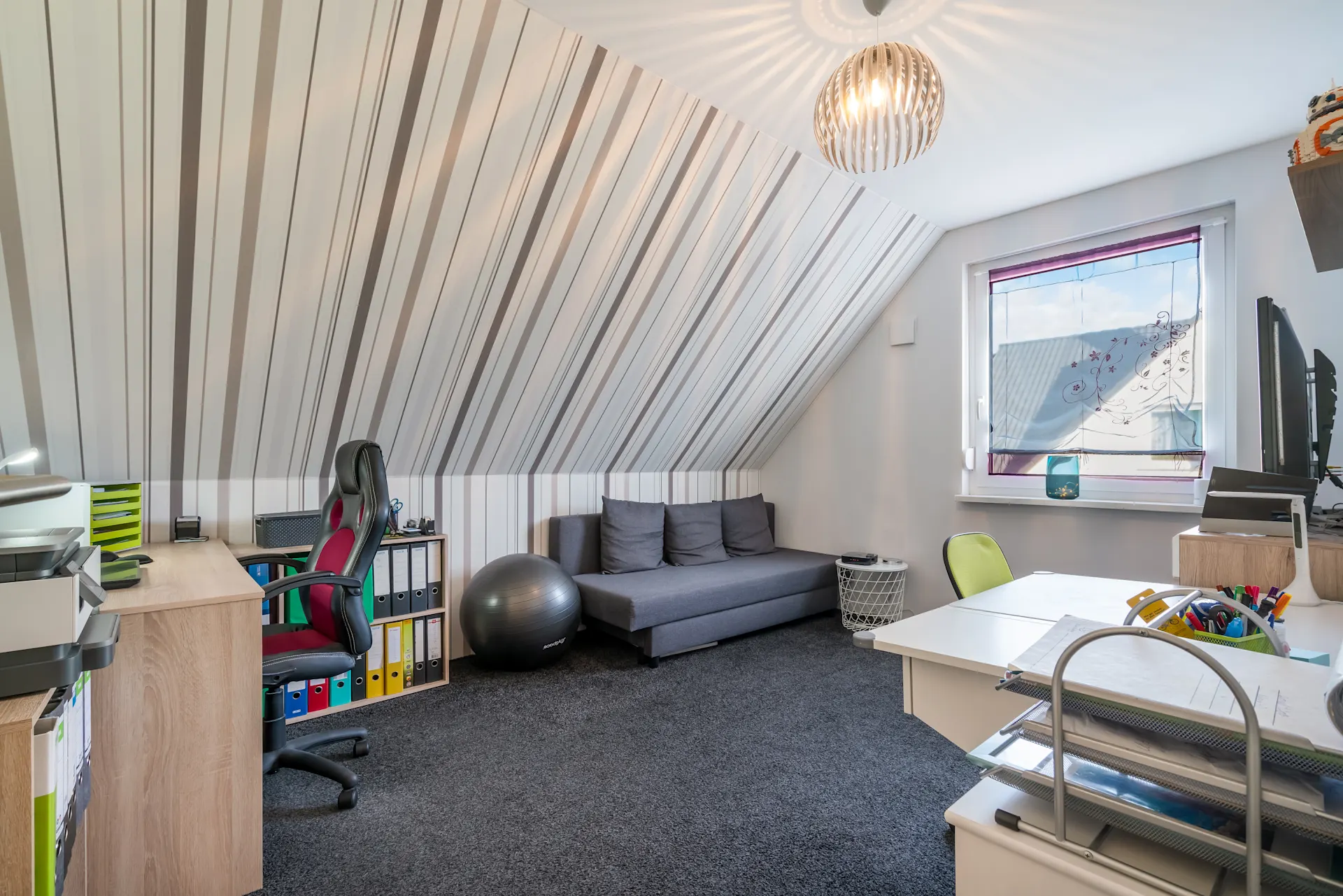Modernes Arbeitszimmer mit Schreibtisch, Sofa, Bürostuhl und Fenster im Dachgeschoss.