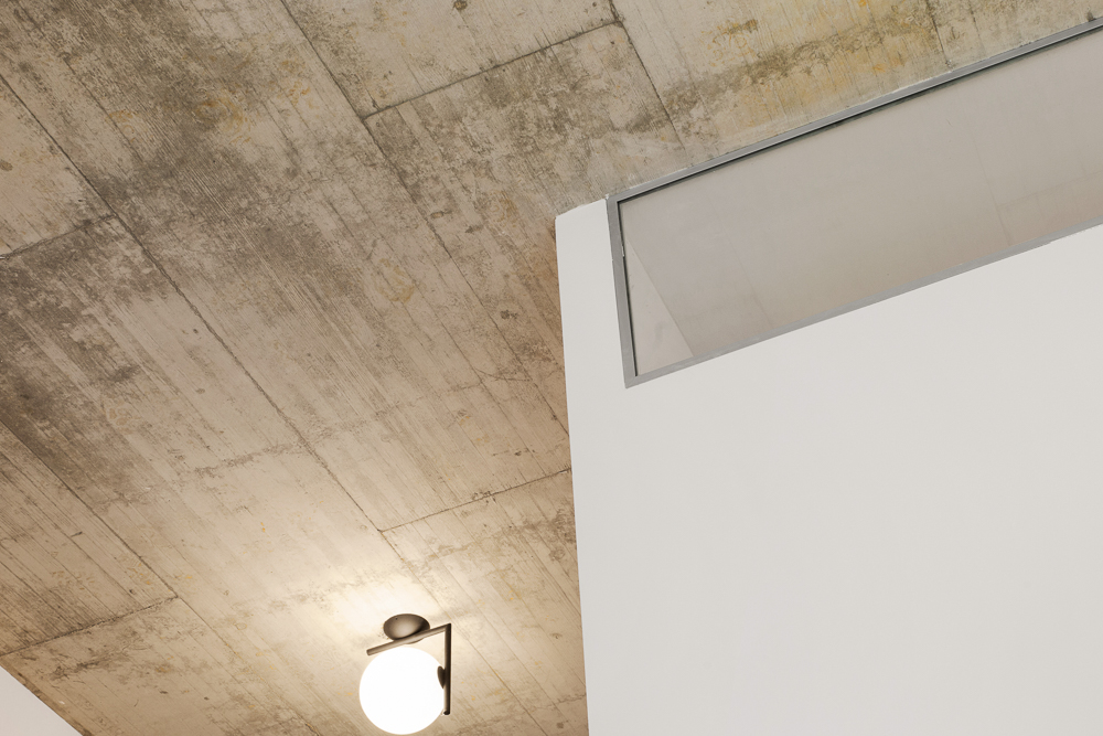 Betondecke mit einer runden Wandlampe und einem Fenster über einer weißen Wand.