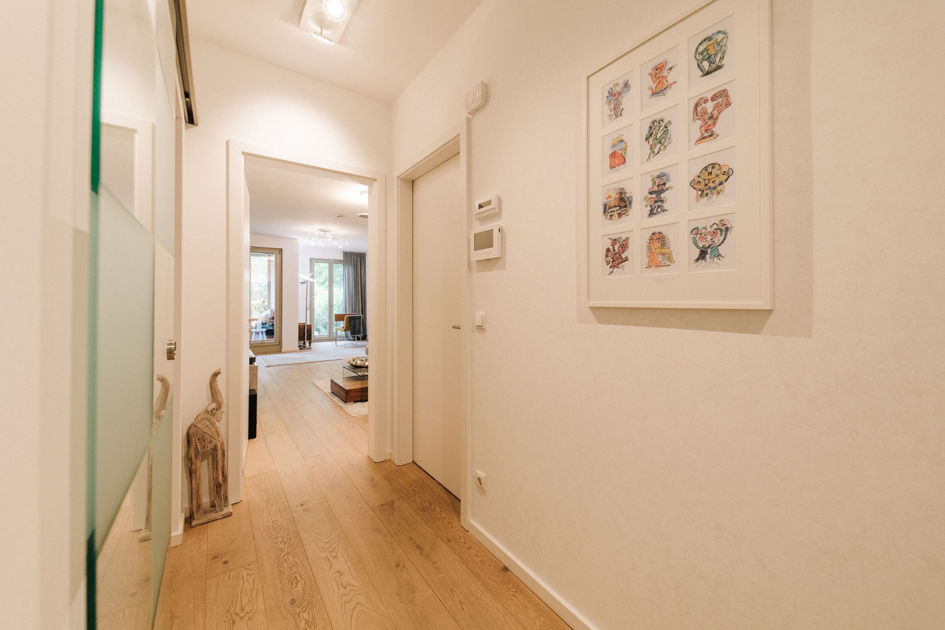 Heller Flur mit Holzboden, Kunst an der Wand und Blick ins Wohnzimmer.