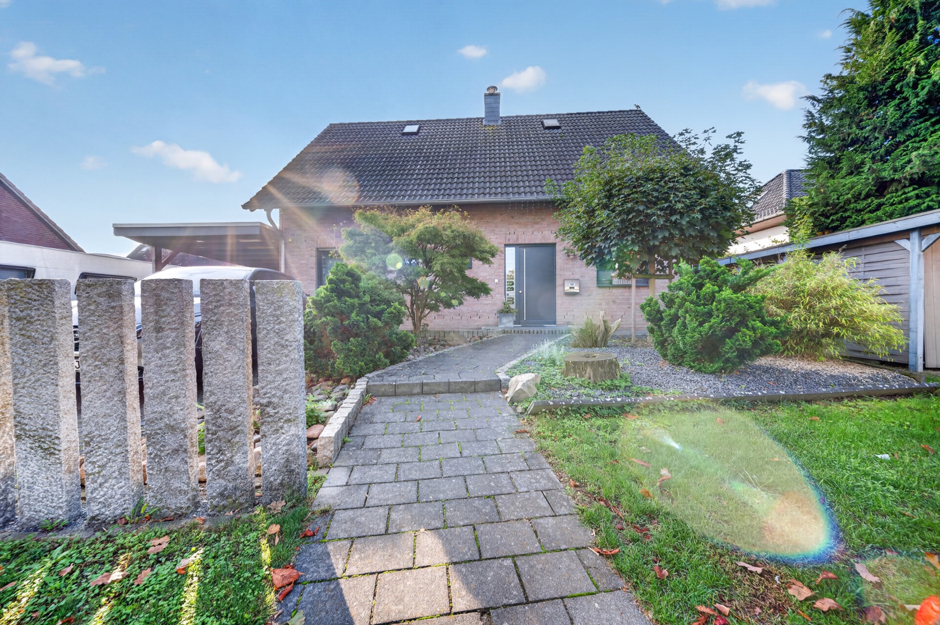 Gepflasterter Weg führt zu einem Einfamilienhaus mit Vorgarten, Bäumen und Garage.