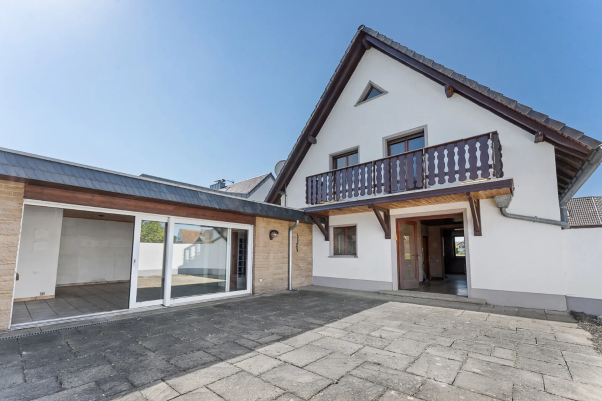 Außenansicht eines Wohnhauses mit Terrasse, Balkon und großen Glas-Schiebetüren.
