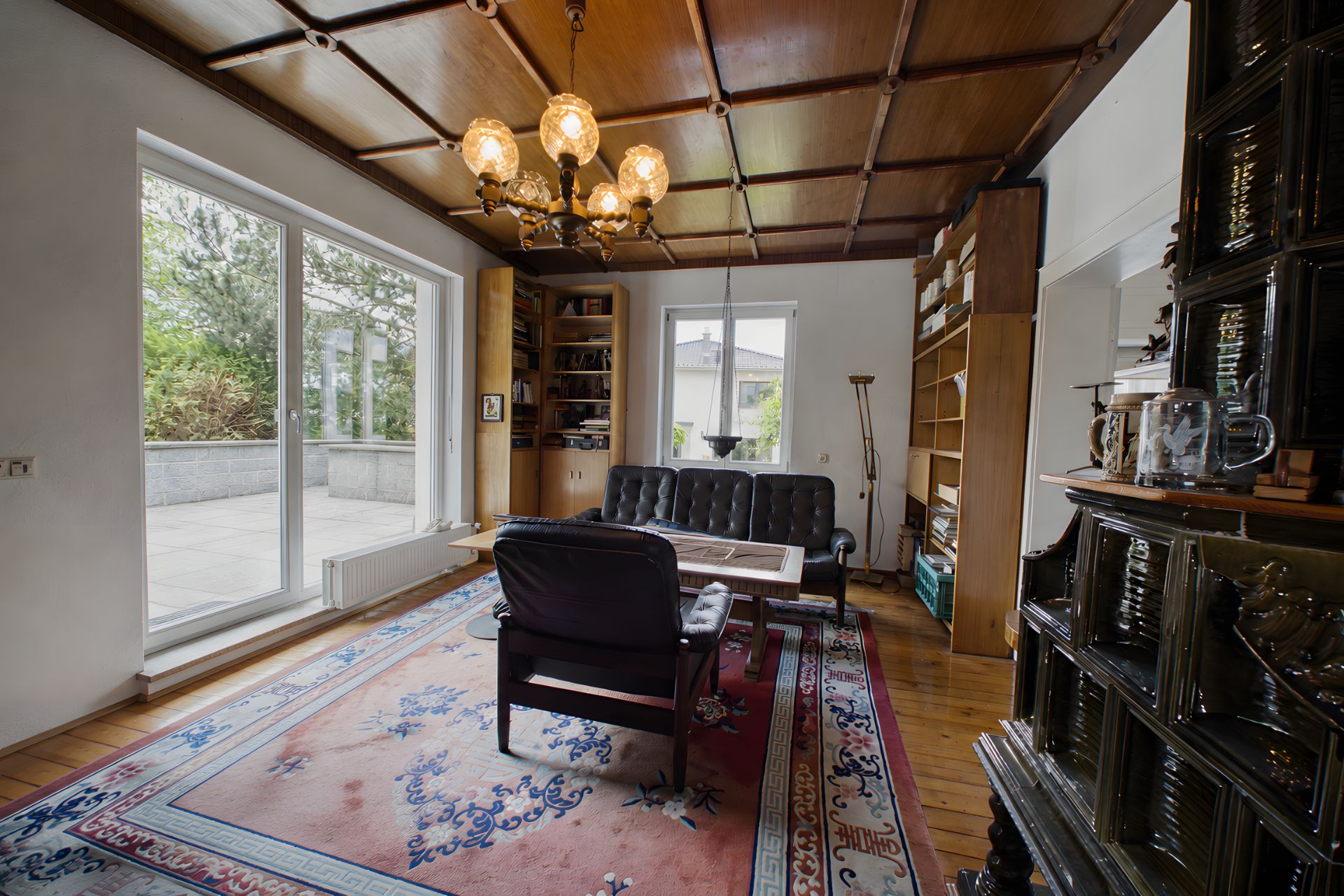 Wohnzimmer mit Teppich, Ledersofas, Bücherregalen, großem Fenster und Kronleuchter.