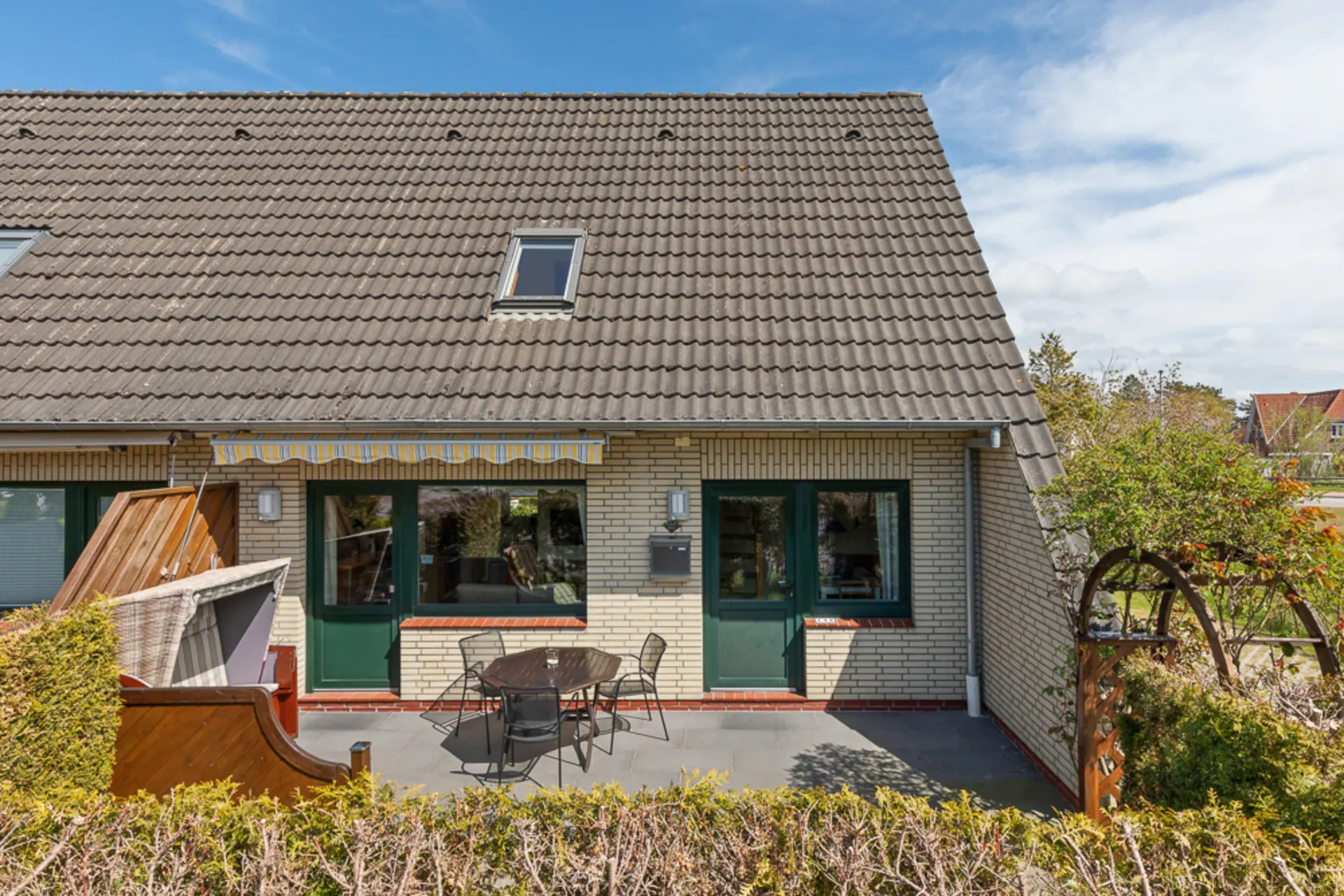 Halbes Einfamilienhaus mit Terrasse, Gartenmöbeln und Markise vor dem Haus.