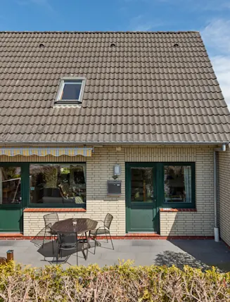 Halbes Einfamilienhaus mit Terrasse, Gartenmöbeln und Markise vor dem Haus.