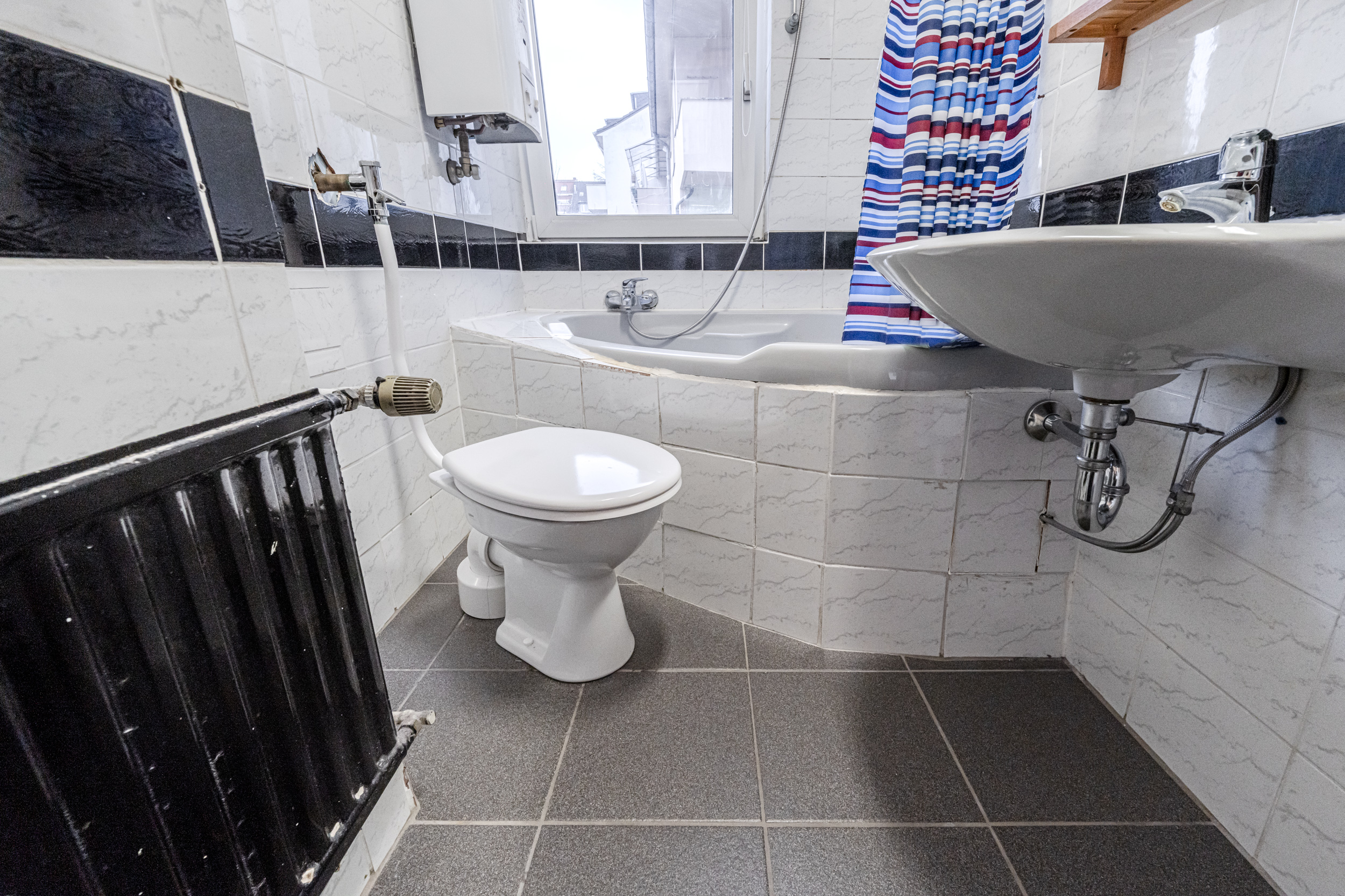 Kleines Badezimmer mit Toilette, Waschbecken, Badewanne und gestreiftem Duschvorhang.