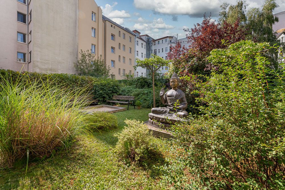 Gepflegter Garten mit Buddha-Statue und Bank, umgeben von Wohngebäuden.