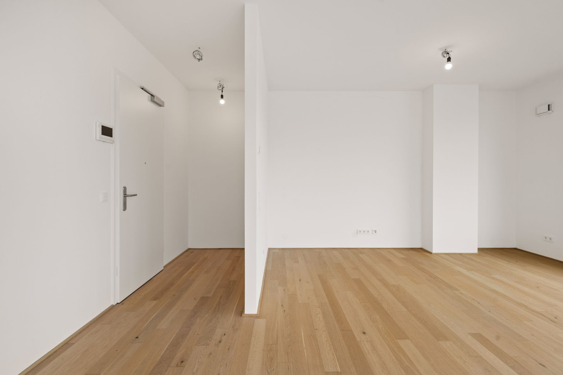 Leerer Raum mit Holzfußboden, weißen Wänden und einer Trennwand.