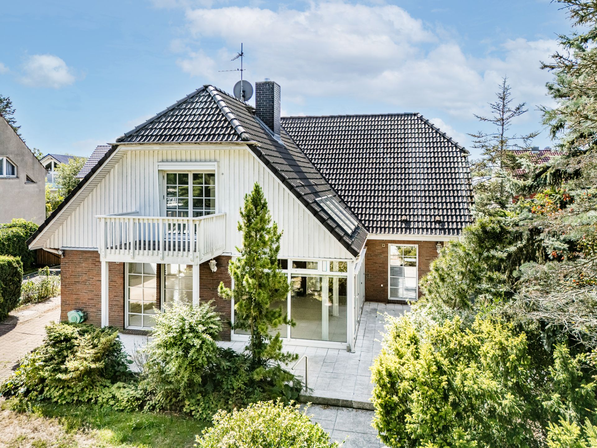 Zweistöckiges Einfamilienhaus mit Balkon, Terrasse und Garten, umgeben von Bäumen.