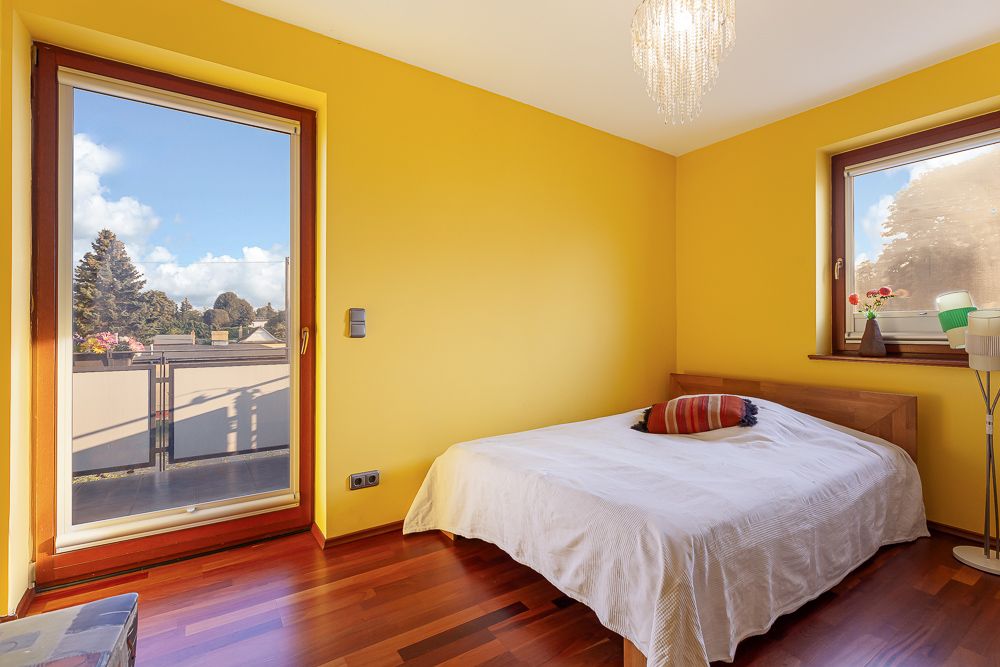 Schlafzimmer mit gelben Wänden, Doppelbett, Fenster und Tür zum Balkon.