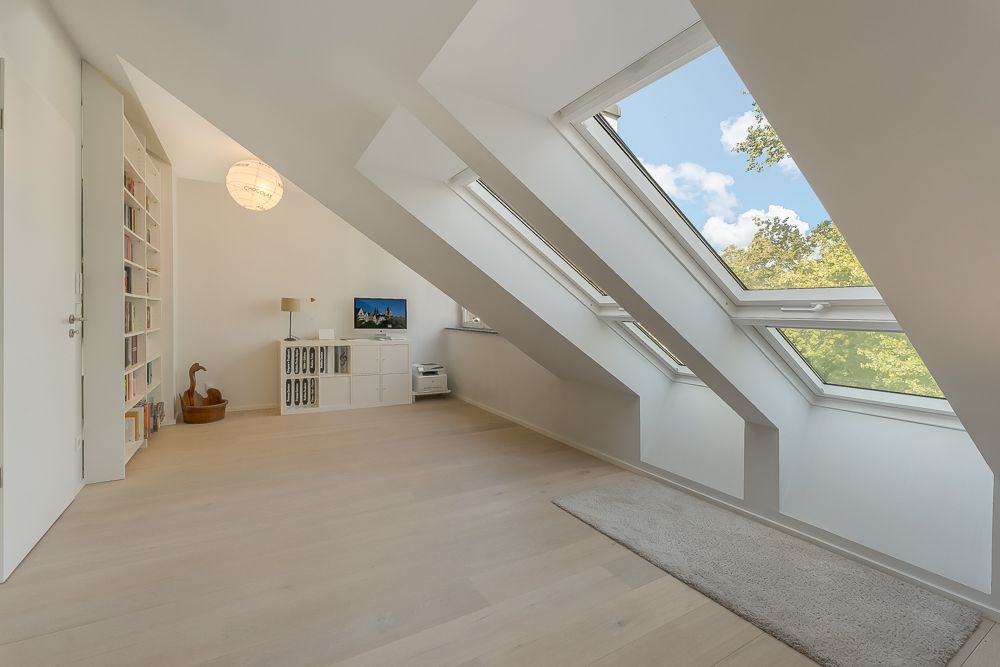 Heller Dachraum mit großen Dachfenstern, Holzfußboden, Regal und TV-Möbel.
