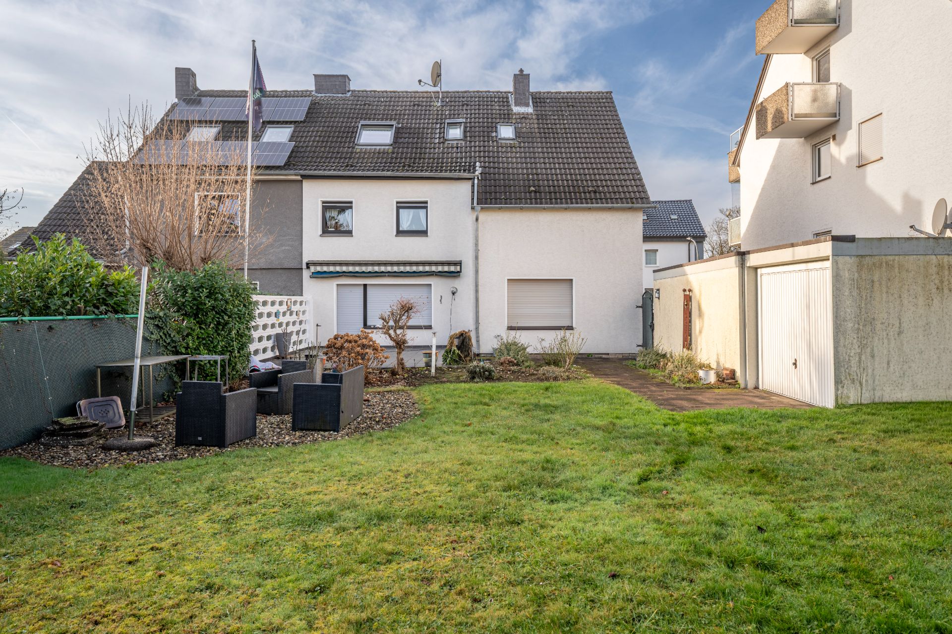 Garten mit Rasenfläche, Sitzgruppe und Blick auf ein Haus mit Terrasse.