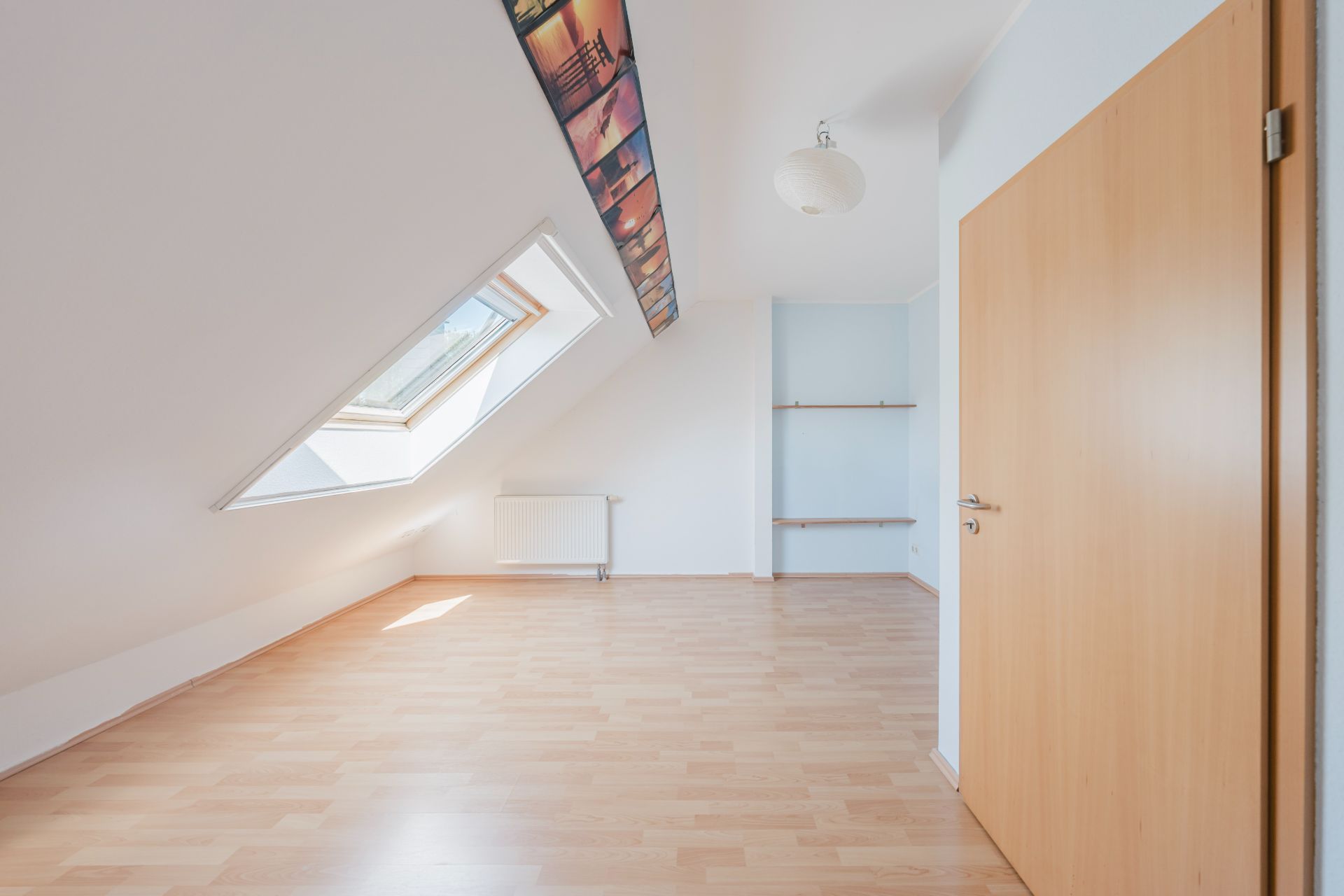 Helles Dachzimmer mit schrägem Fenster, Holzfußboden und Regalen an der Wand.