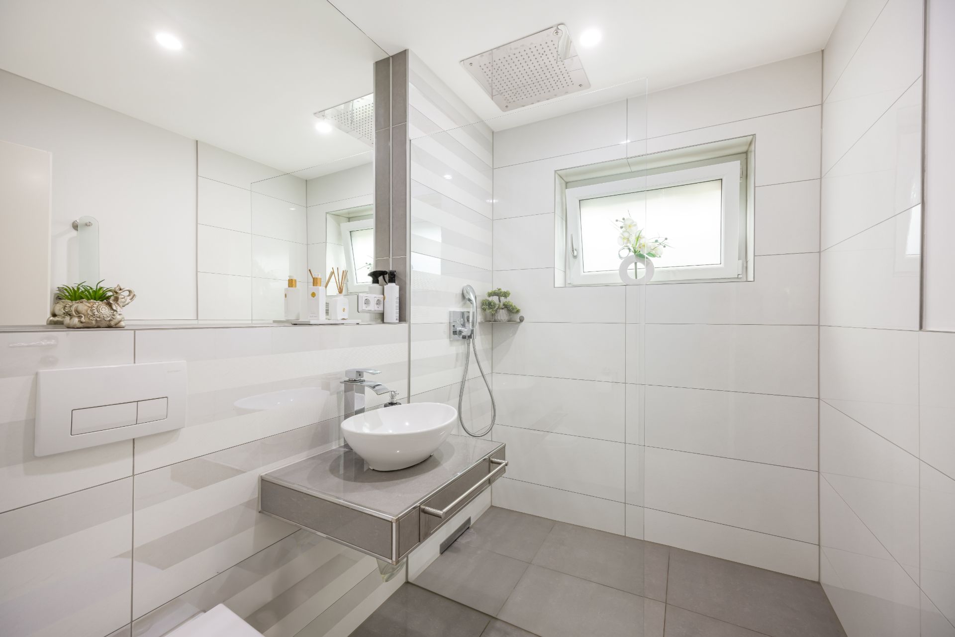 Modernes Badezimmer mit ebenerdiger Dusche, Waschbecken und Wandspiegel, hell gefliest.