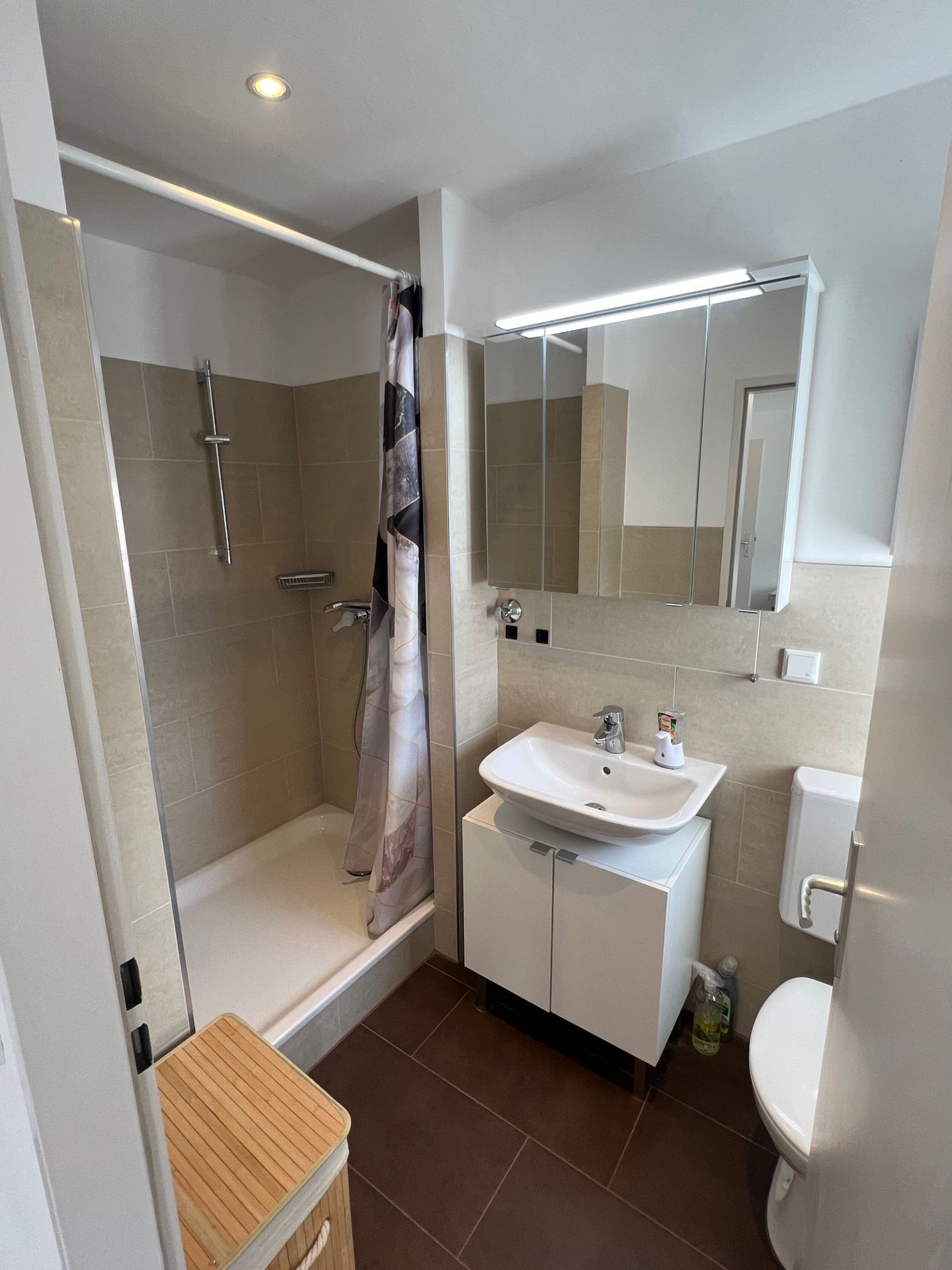 Modernes Badezimmer mit Dusche, Waschbecken, Spiegel, Toilette und Wäschekorb.
