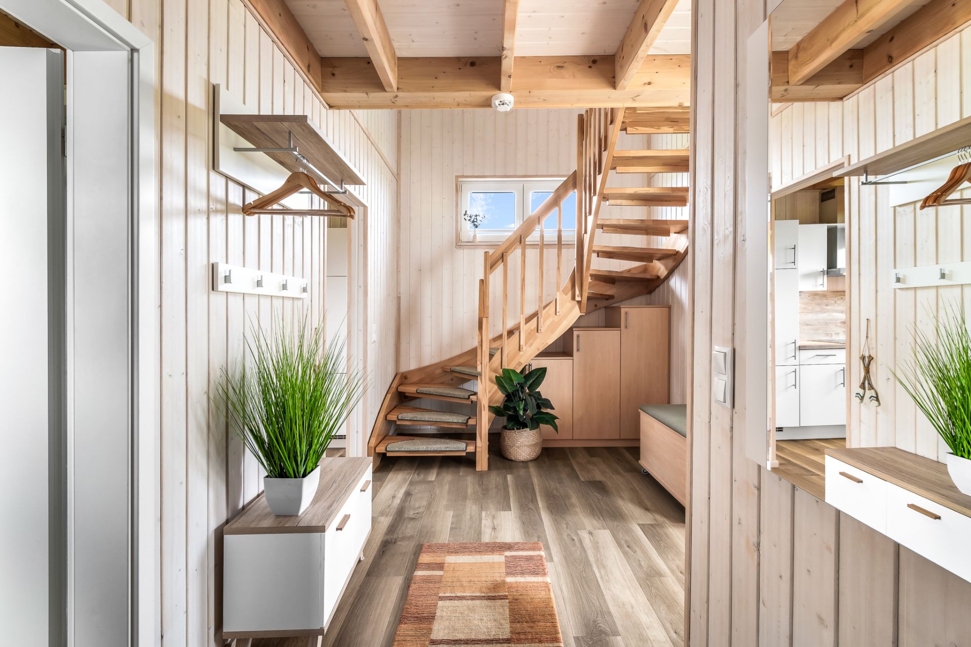 Heller Flur mit Holztreppe, Pflanzen, Garderobe und Spiegel.
