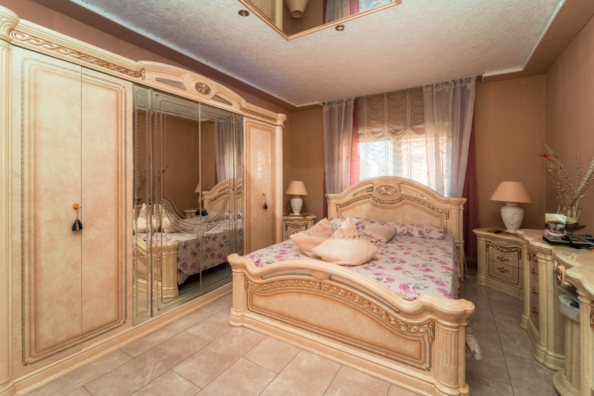 Schlafzimmer mit hellem Holzbett, großem Kleiderschrank mit Spiegeln und Nachttischen.