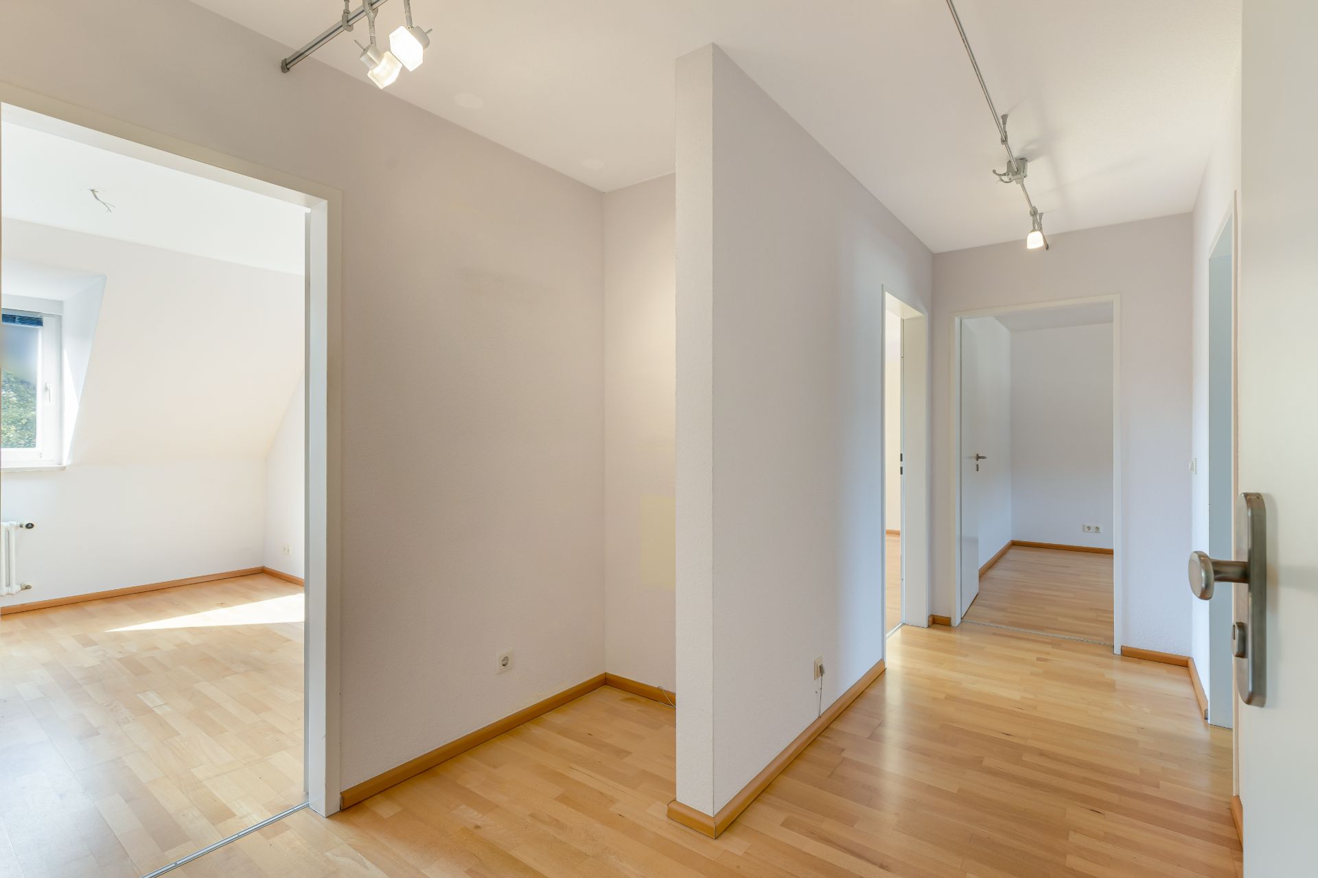 Heller Flur mit Holzboden, mehreren Türen und weißen Wänden in einer Wohnung.