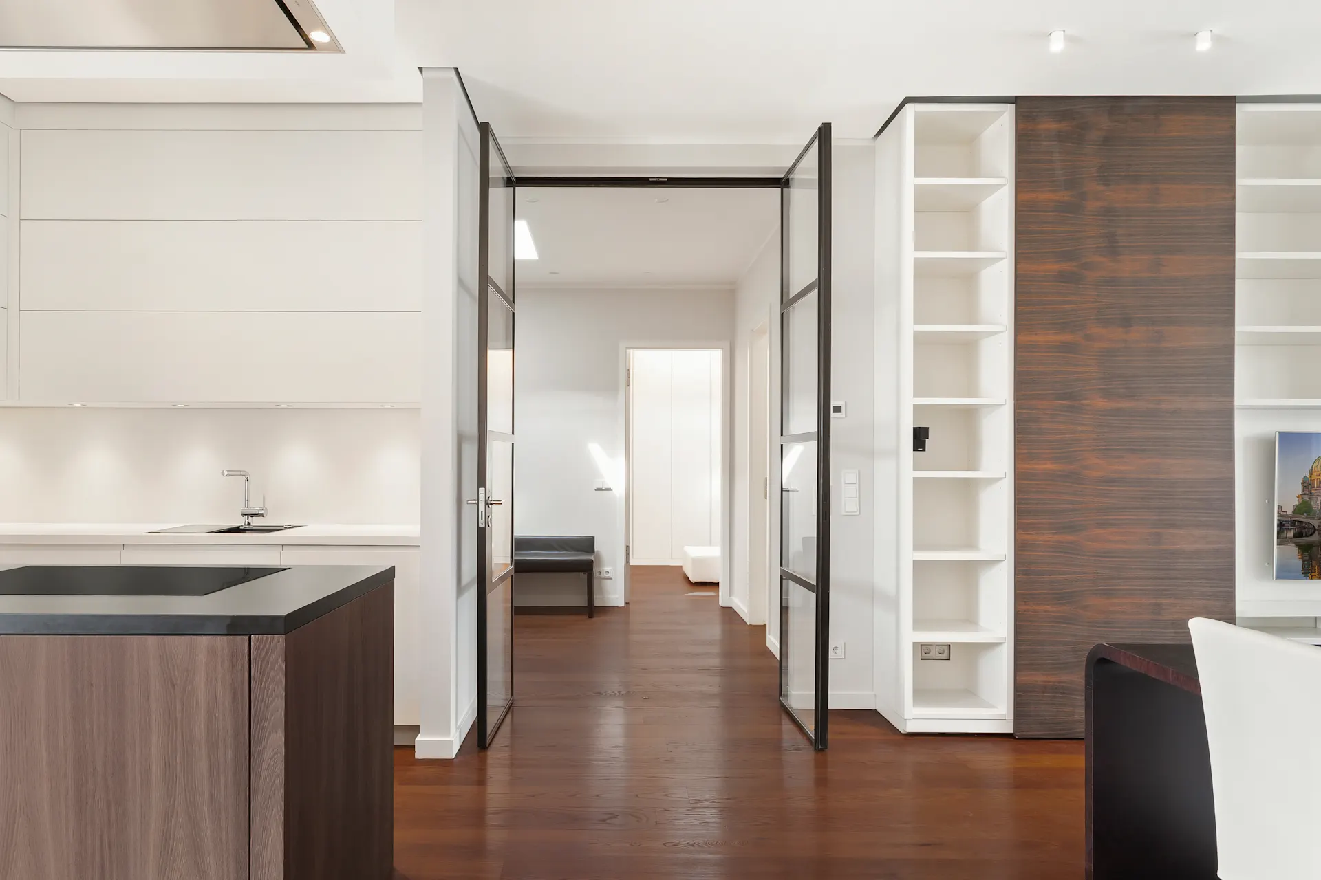 Moderne, helle Küche mit Holzboden und offenem Durchgang zu einem Flur mit Regalen.