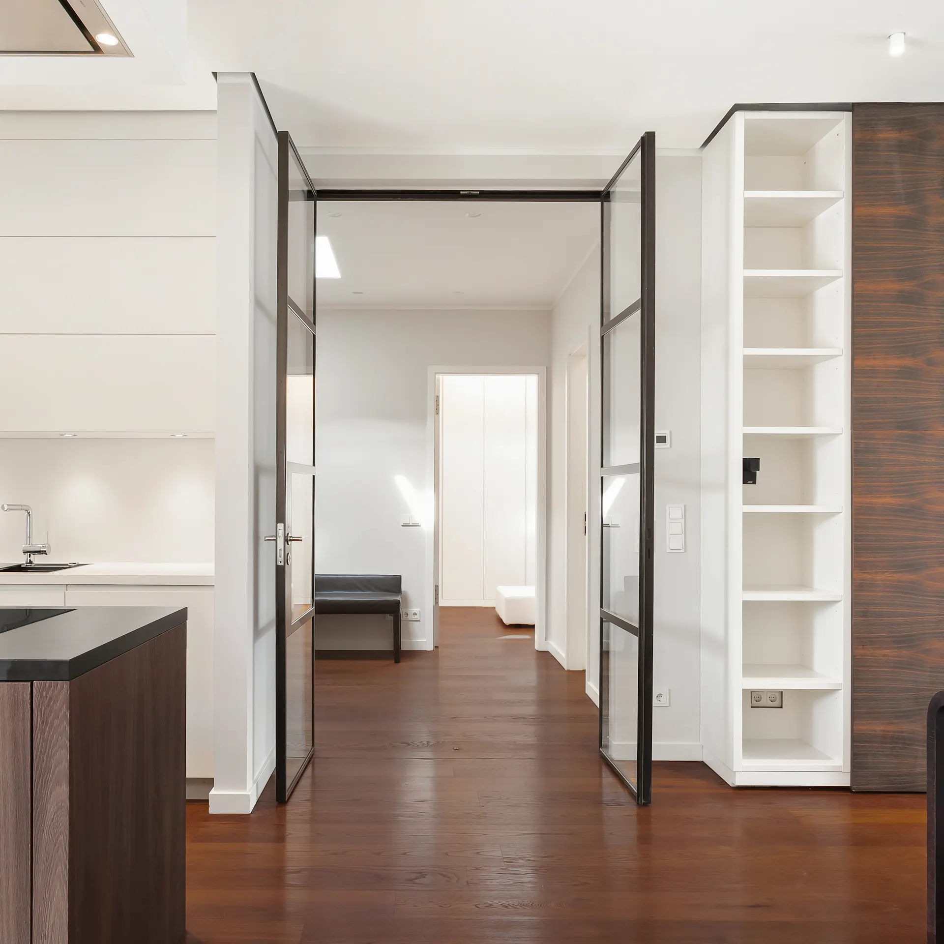 Moderne, helle Küche mit Holzboden und offenem Durchgang zu einem Flur mit Regalen.