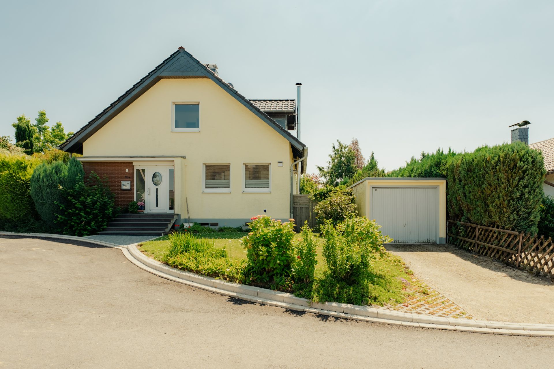 Einfamilienhaus mit Garten, Garage und Auffahrt, umgeben von Grünpflanzen.