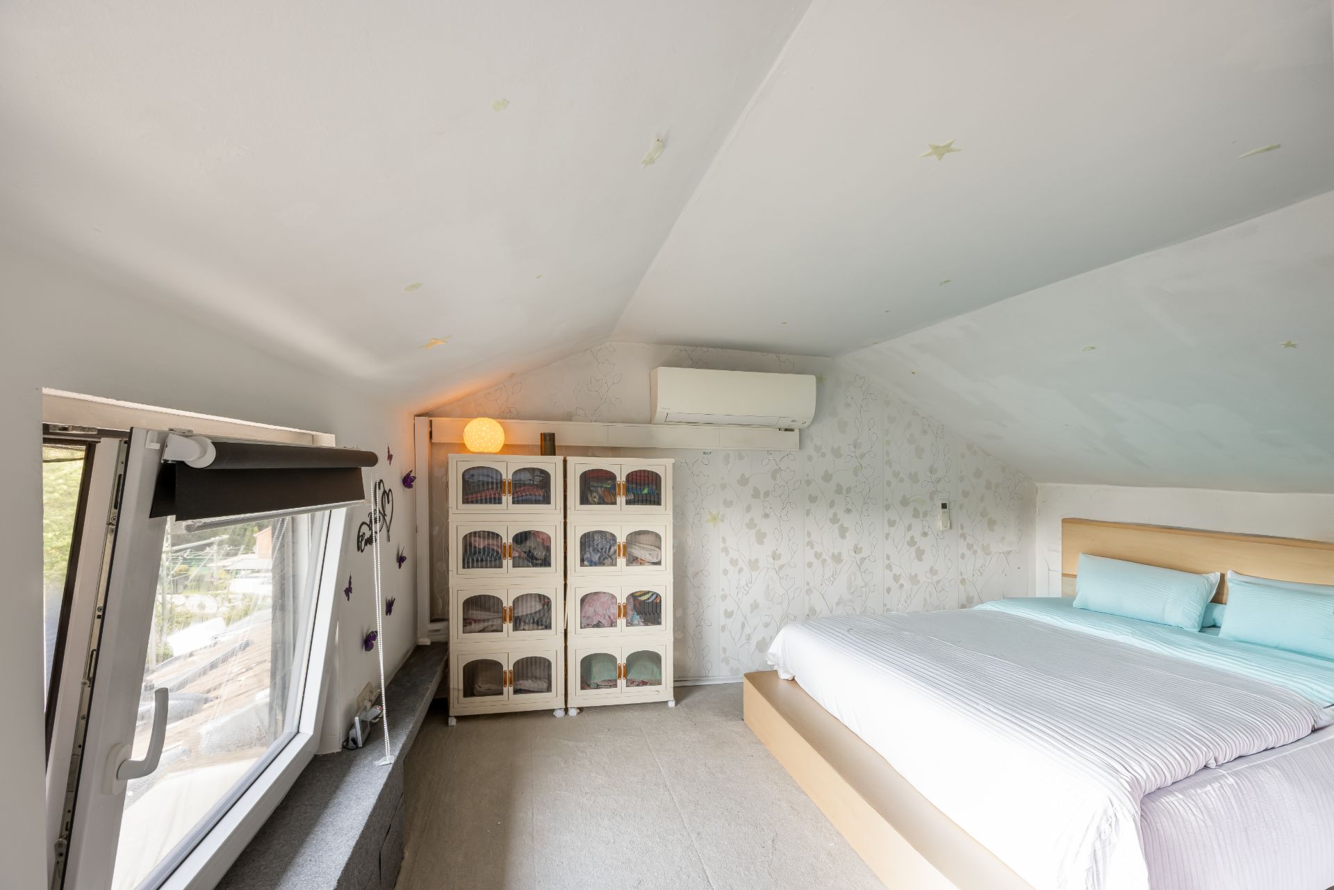 Schlafzimmer mit Dachschräge, Bett, Kommode und Fenster mit Blick nach draußen.