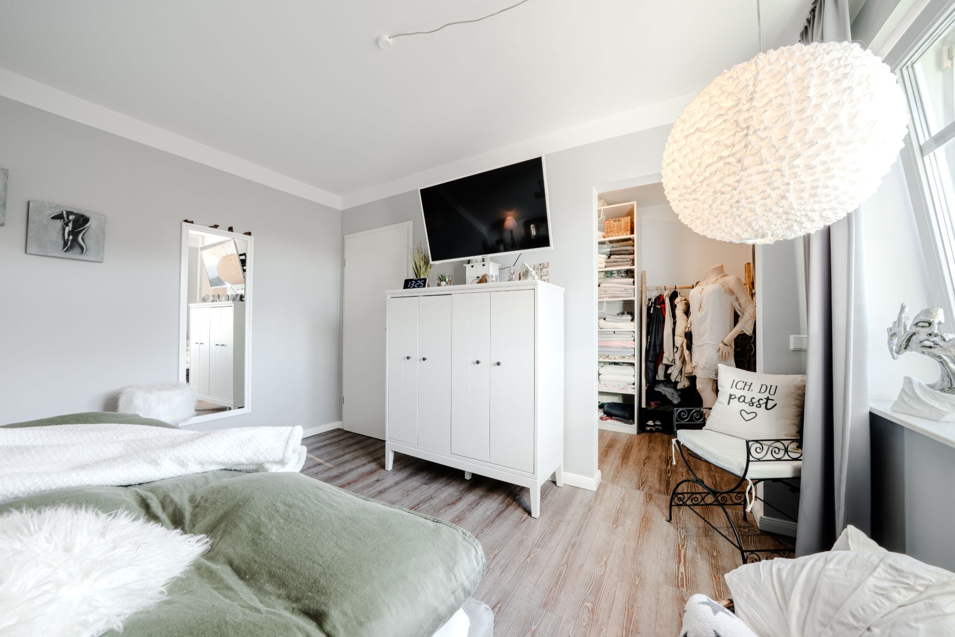 Helles Schlafzimmer mit Schrank, Fernseher, großem Fenster und offenem Zugang zum Ankleidezimmer.