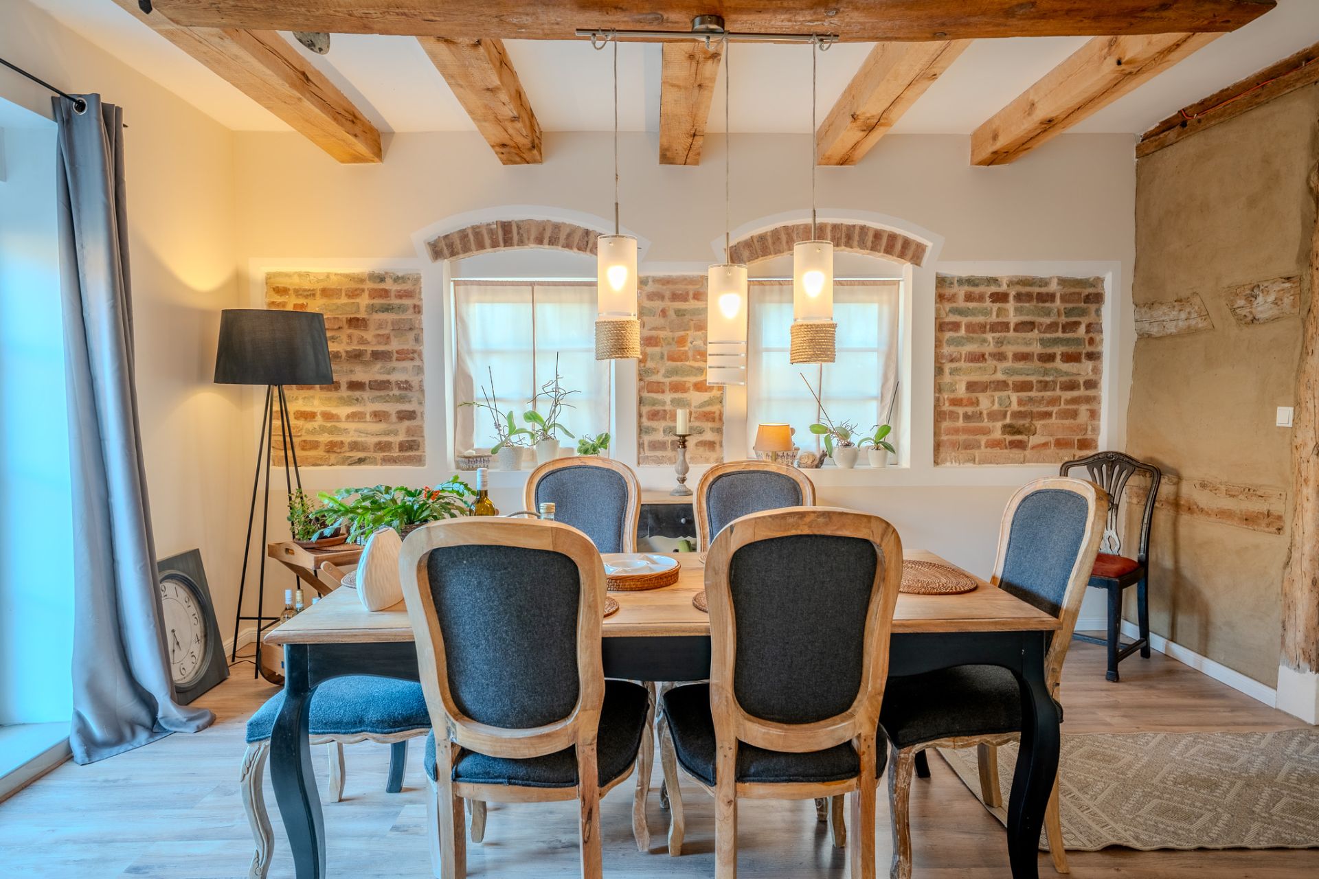 Esszimmer mit Holztisch, sechs Stühlen, Hängelampen und Ziegelwand im Hintergrund.