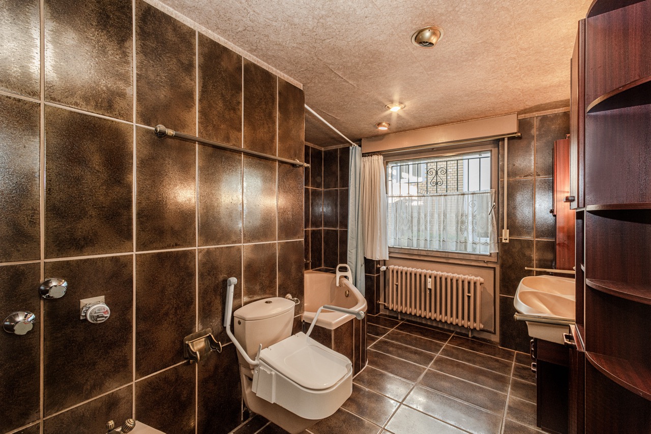 Barrierefreies Badezimmer mit Haltegriffen, Dusche, WC, Waschbecken und Fenster mit Gitter.
