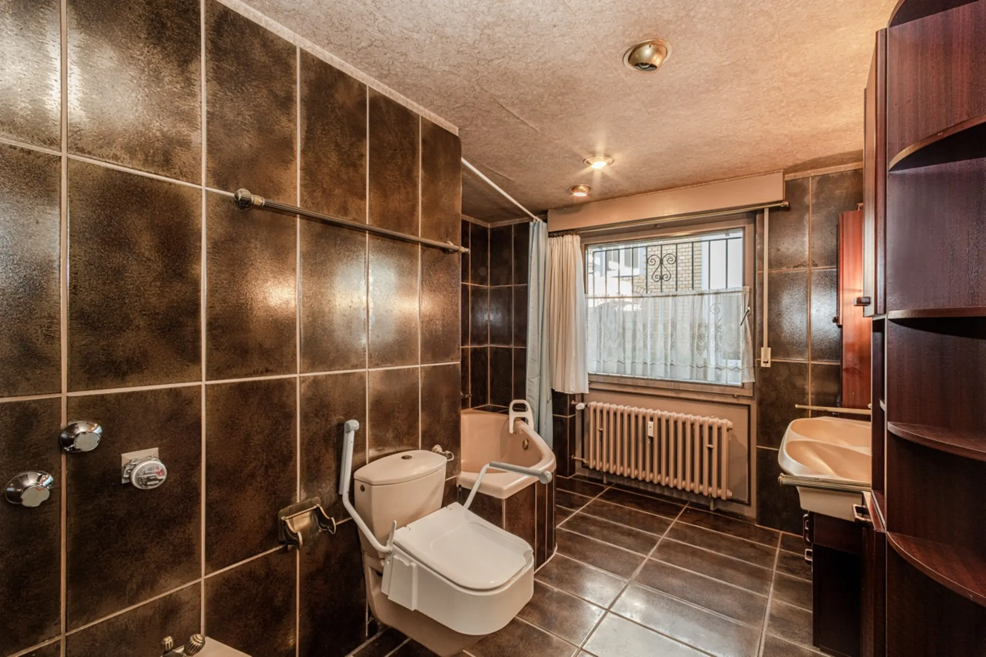 Barrierefreies Badezimmer mit Haltegriffen, Dusche, WC, Waschbecken und Fenster mit Gitter.