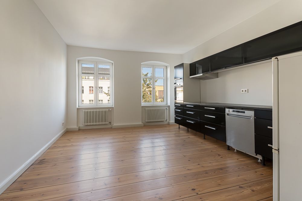 Helle Küche mit Holzboden, zwei Fenstern, schwarzen Schränken und Spülmaschine.