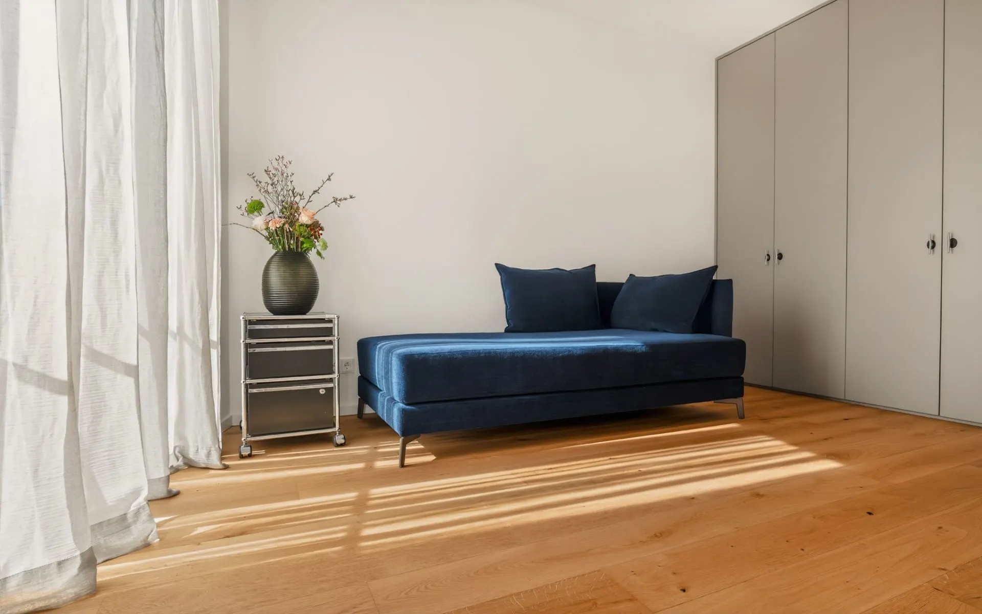 Helles Zimmer mit blauem Sofa, Beistelltisch mit Vase und großem Einbauschrank.