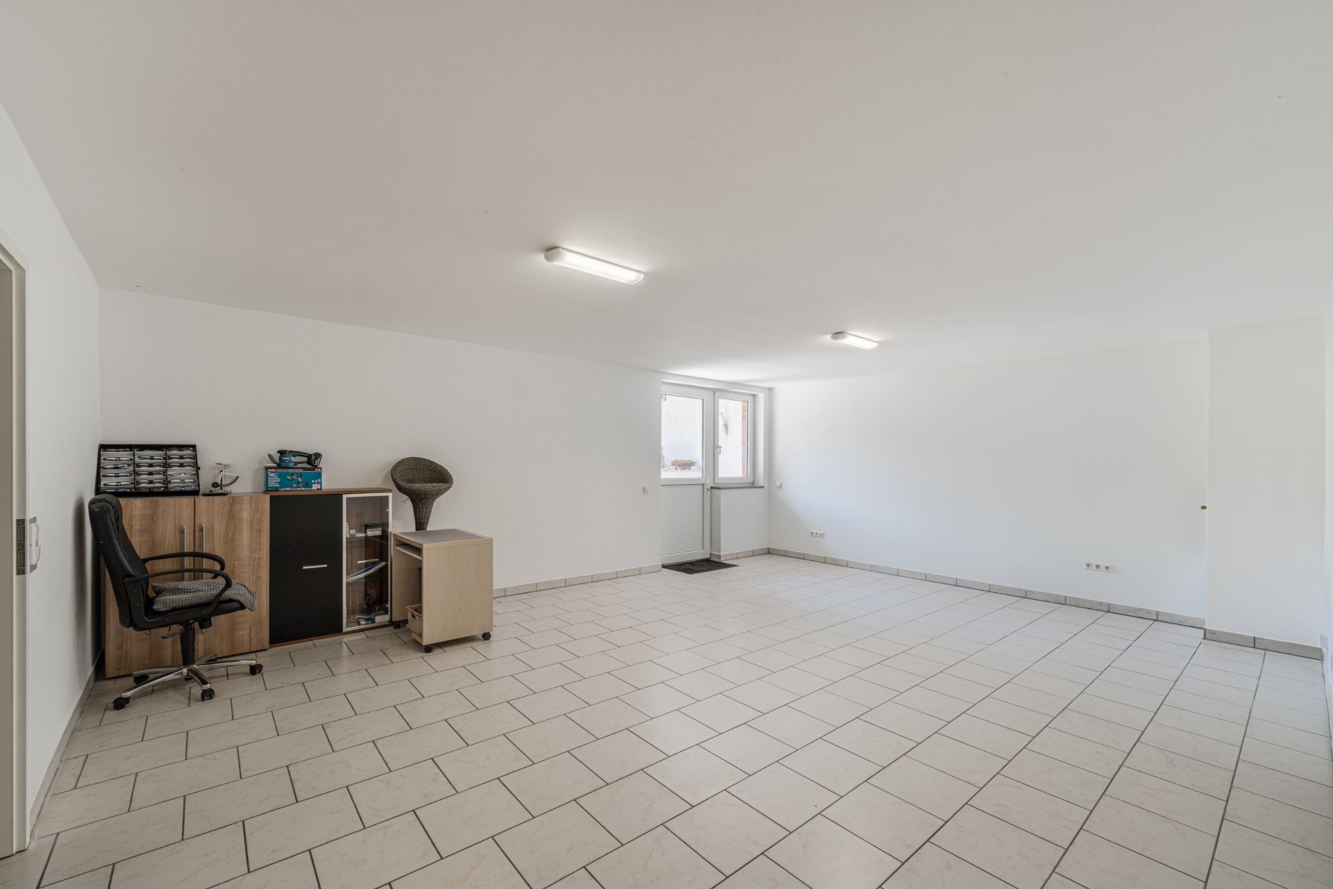 Heller Raum mit Fliesenboden, Schreibtisch, Stuhl und Schränken an der Wand.