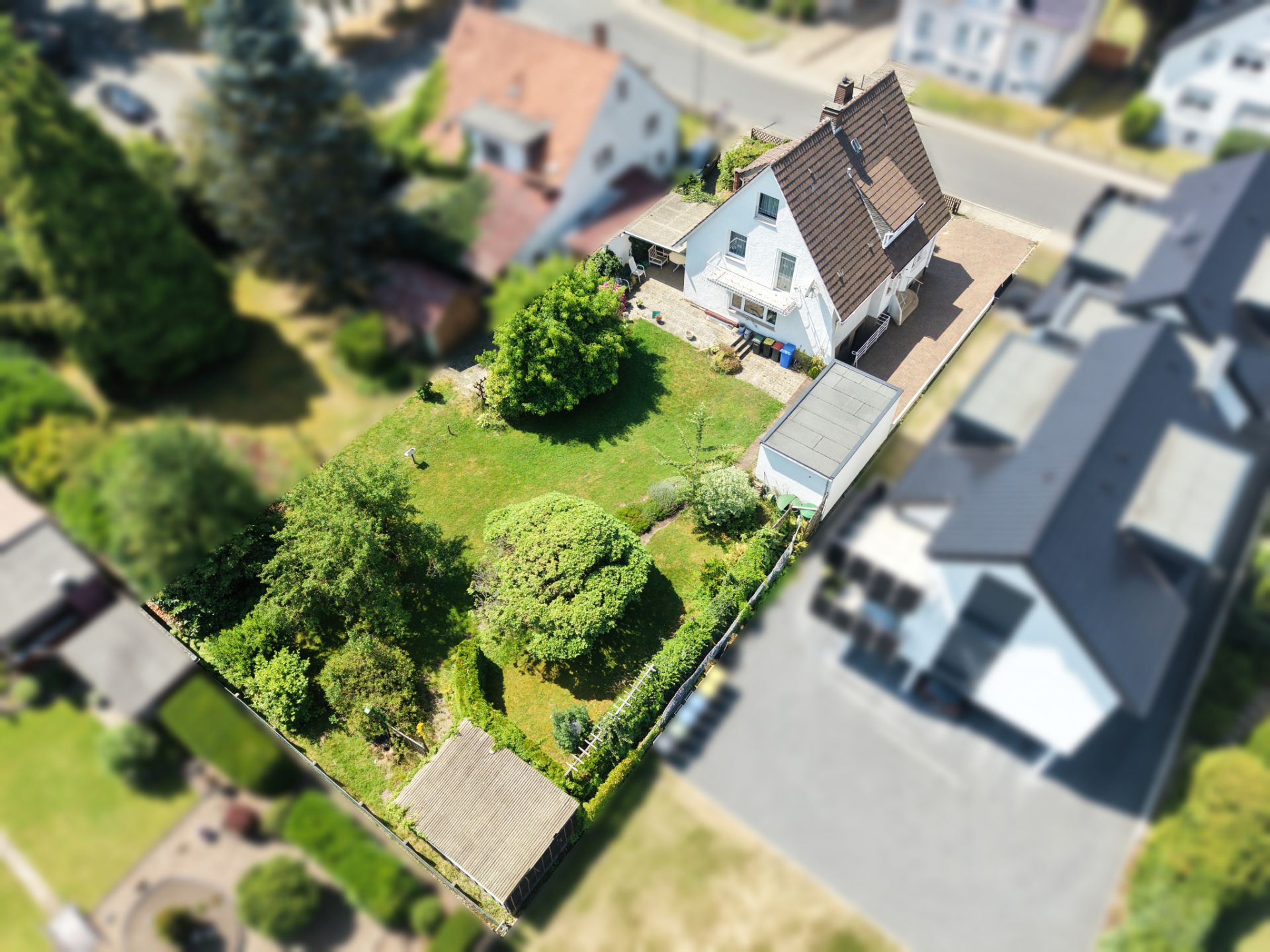 Luftaufnahme eines Hauses mit großem Garten, Rasenfläche, Bäumen und Terrasse, umgeben von Nachbarhäusern.